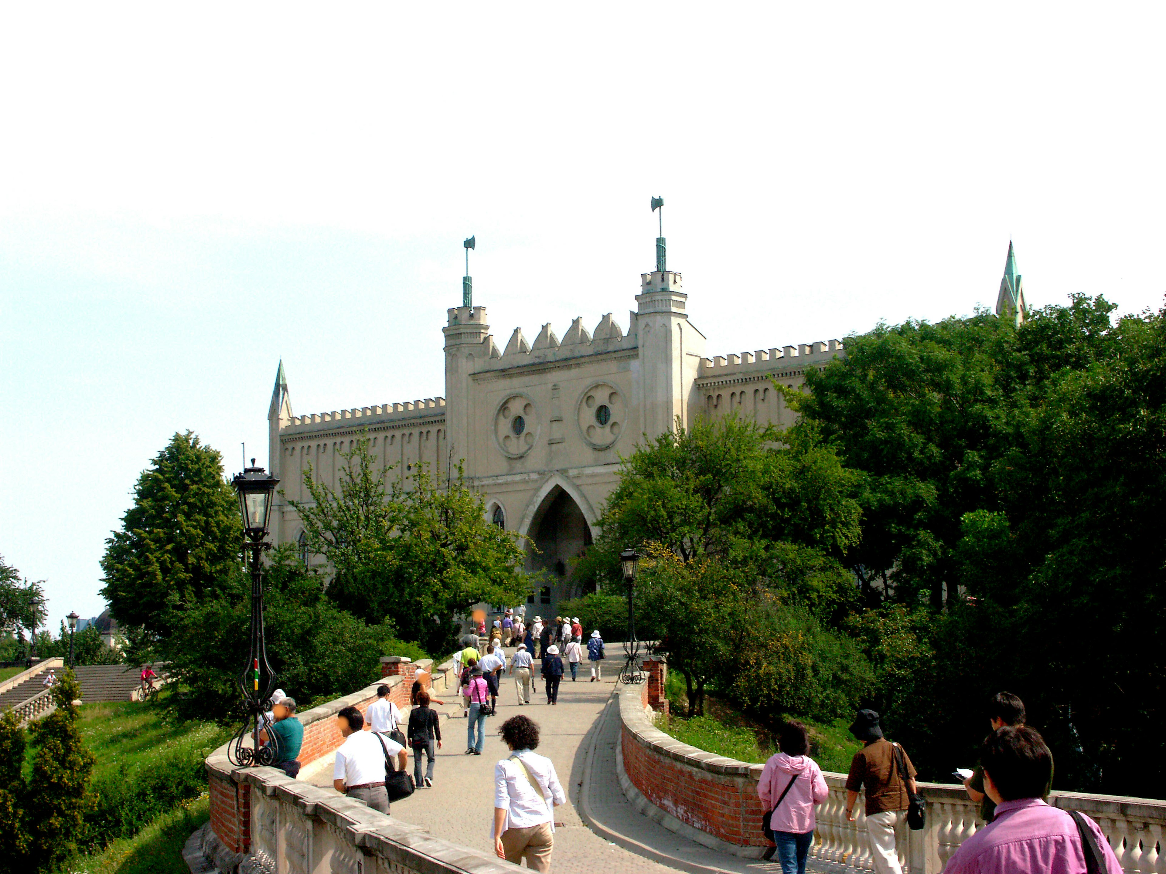 People walking towards a castle entrance surrounded by greenery