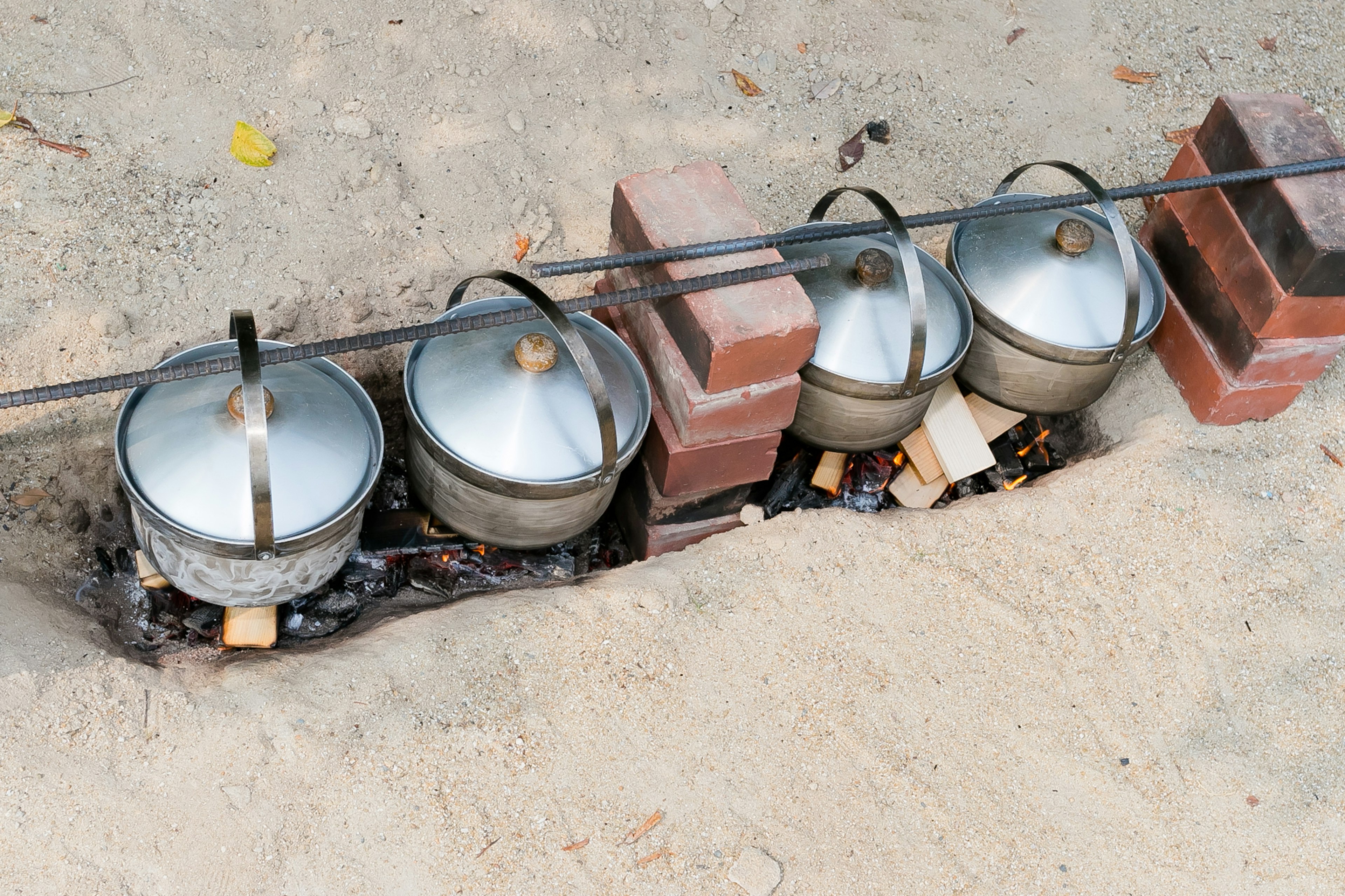 Four pots on a brick stove placed on sandy ground