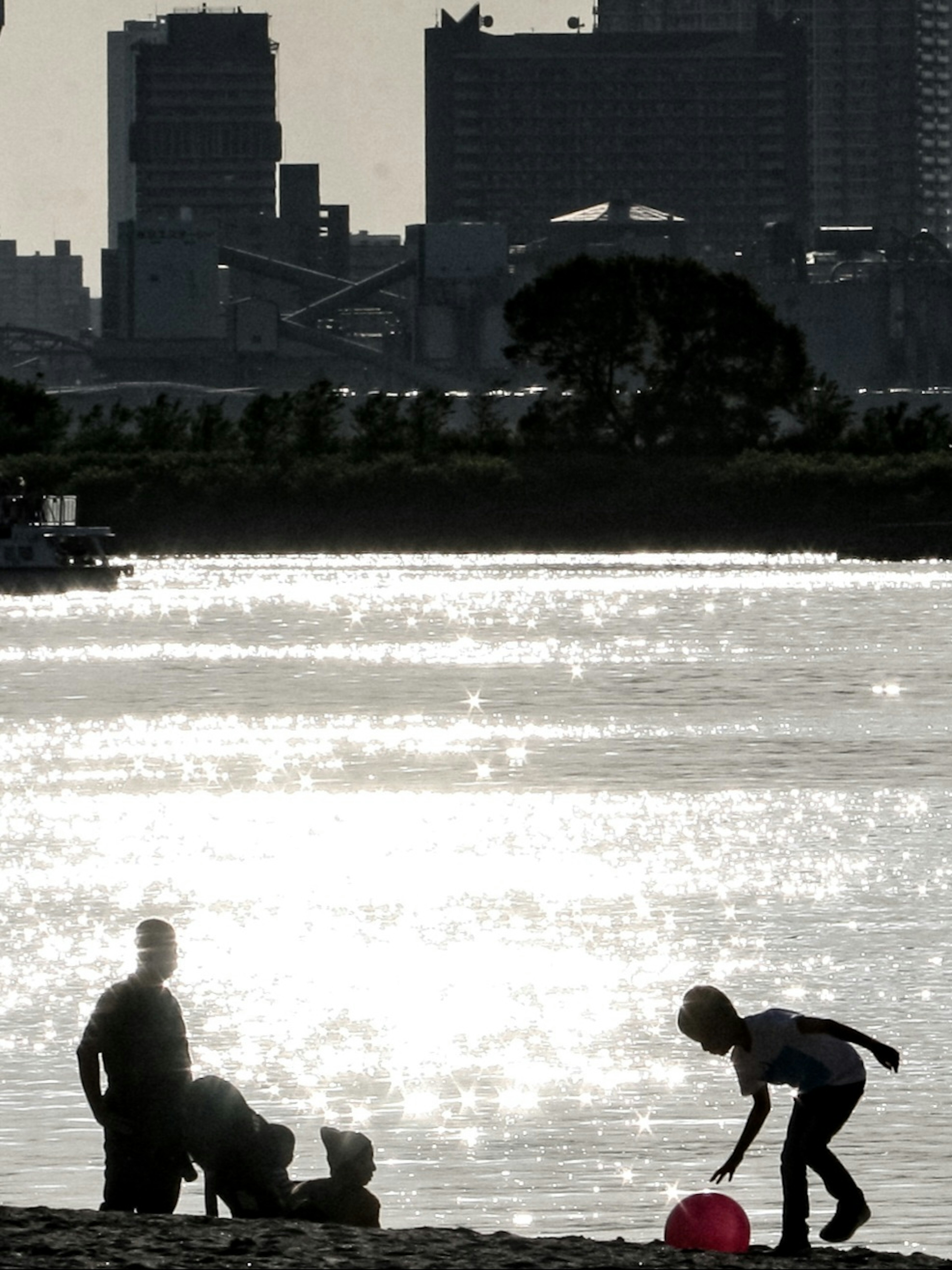 Siluetas de niños y adultos jugando junto al río al atardecer