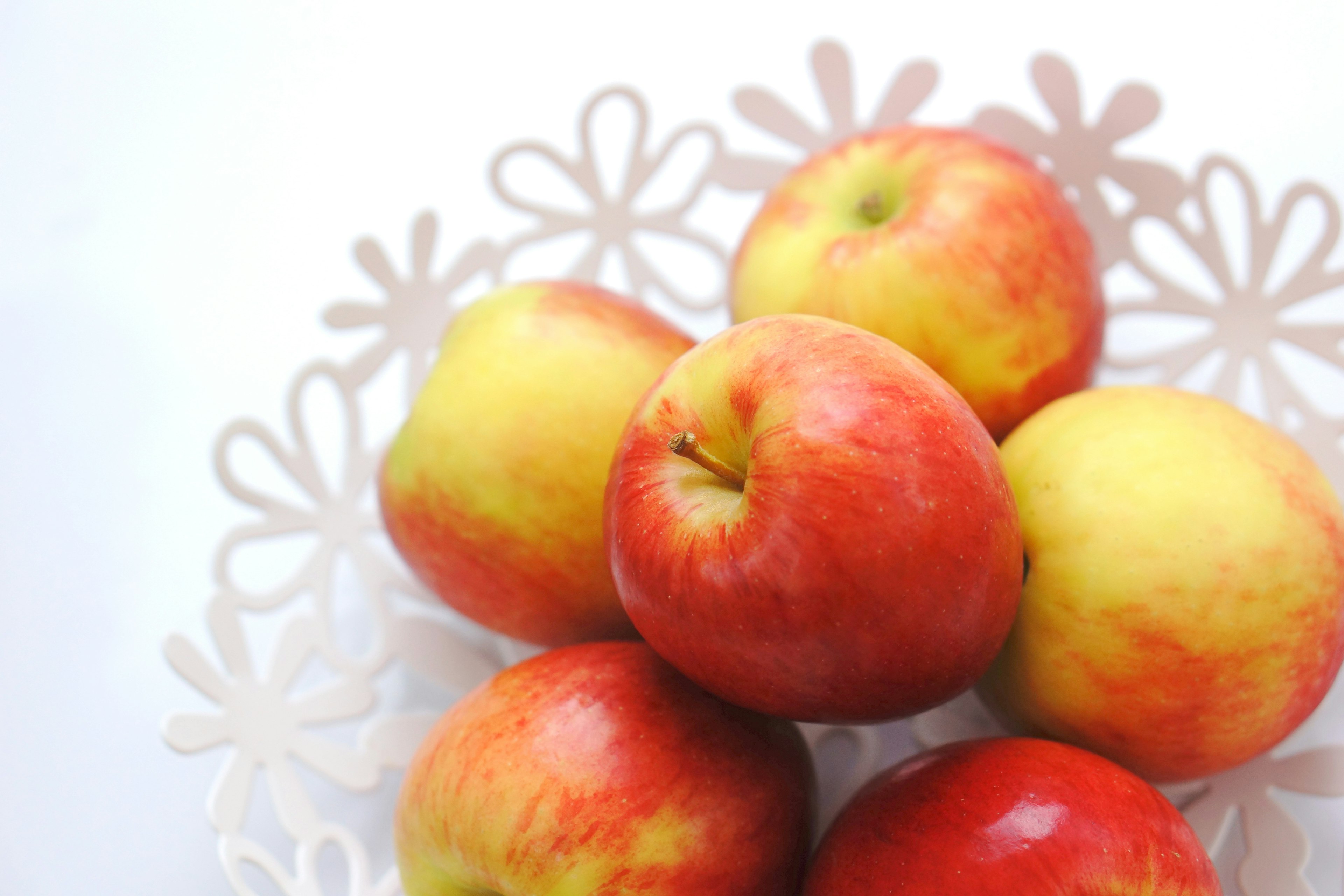 Red and yellow apples arranged in a white floral bowl