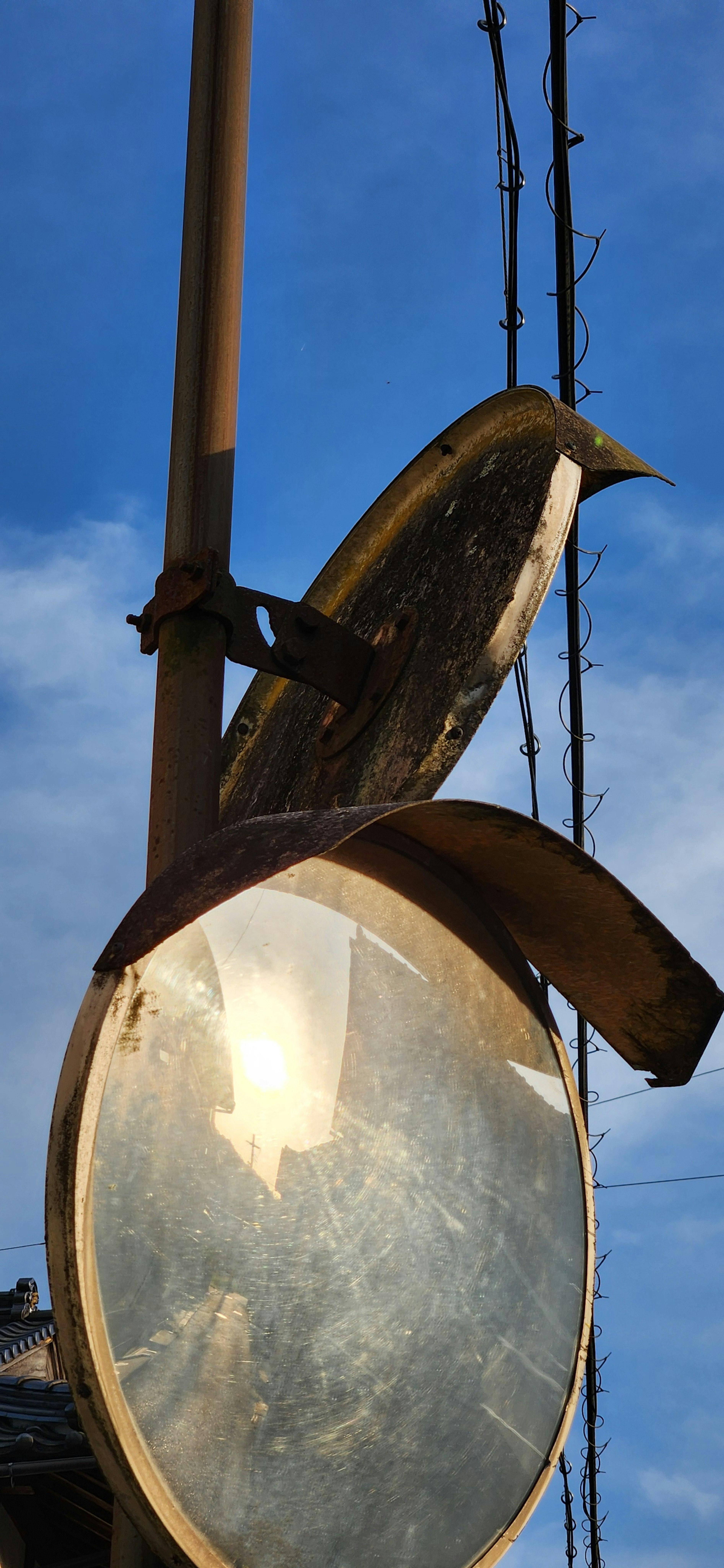 Espejo de señalización antiguo reflejando la luz del sol bajo un cielo azul