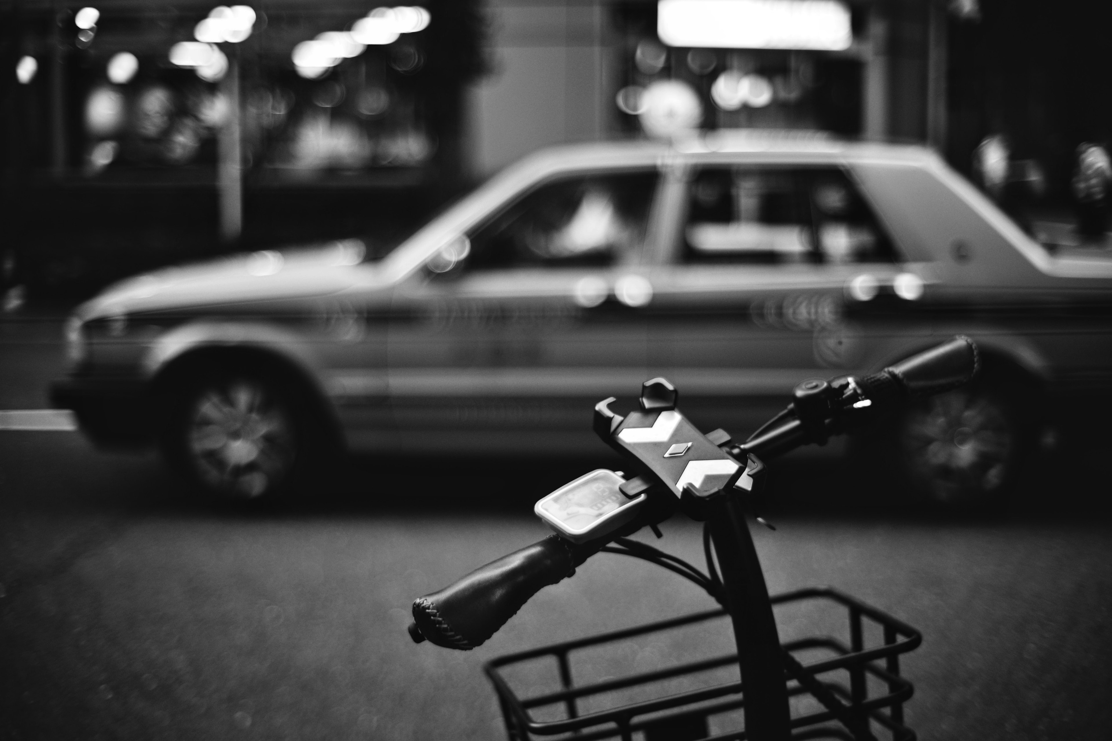 Close-up of a bicycle handlebar and basket with a blurred taxi in the background