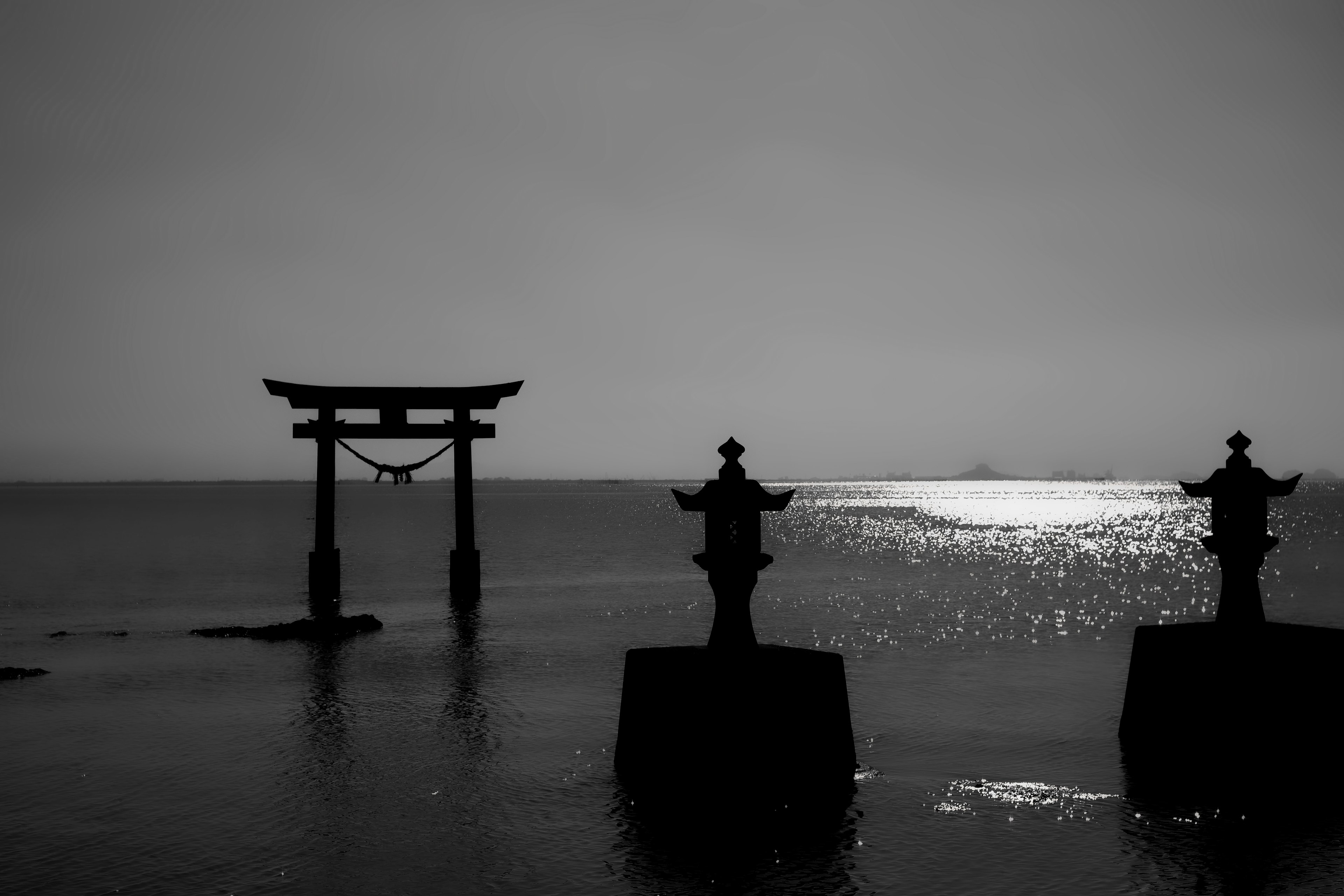 Paisaje marino en blanco y negro con un torii y faroles de piedra