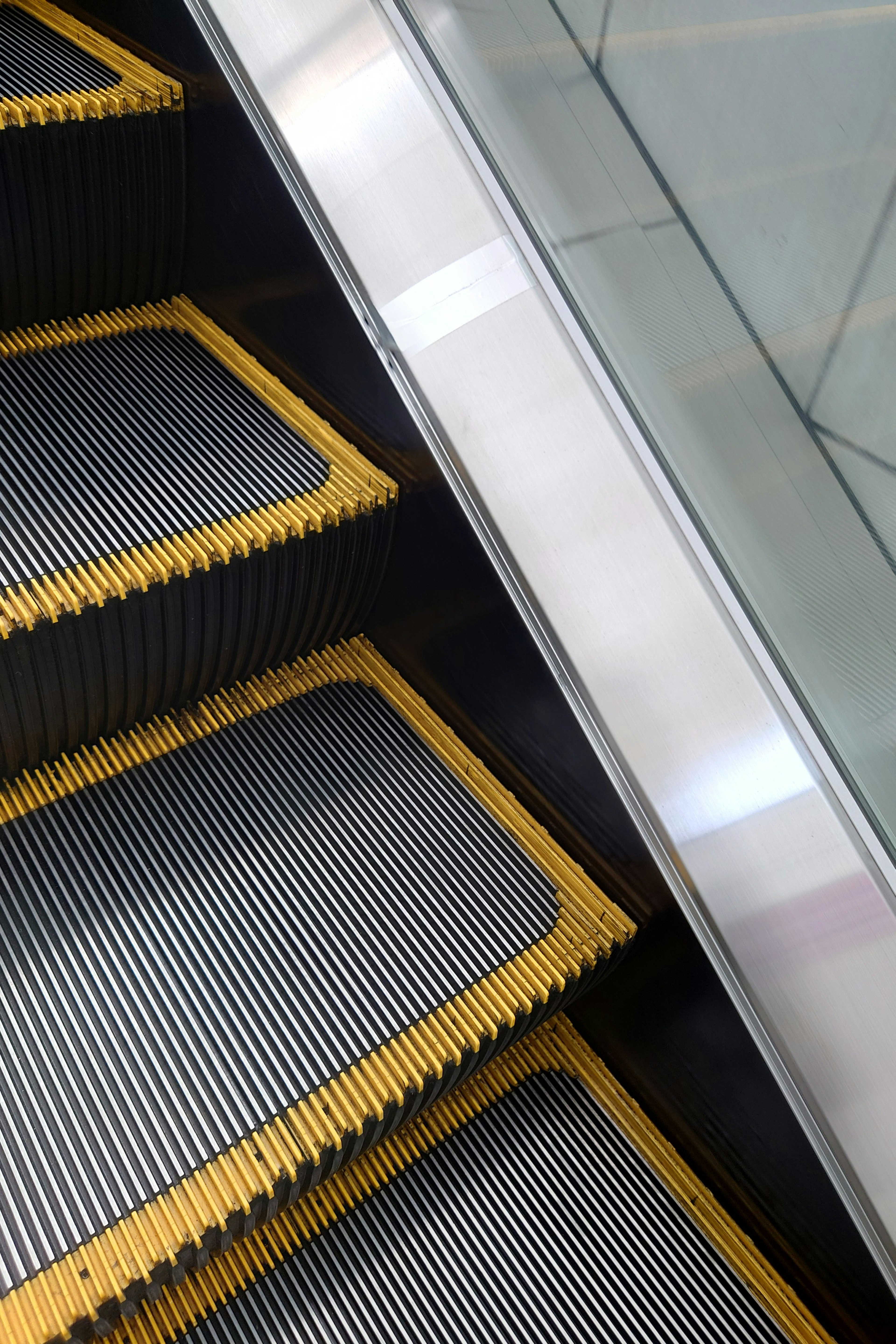 Vista cercana de los escalones de una escalera mecánica con bordes amarillos y barandilla de vidrio