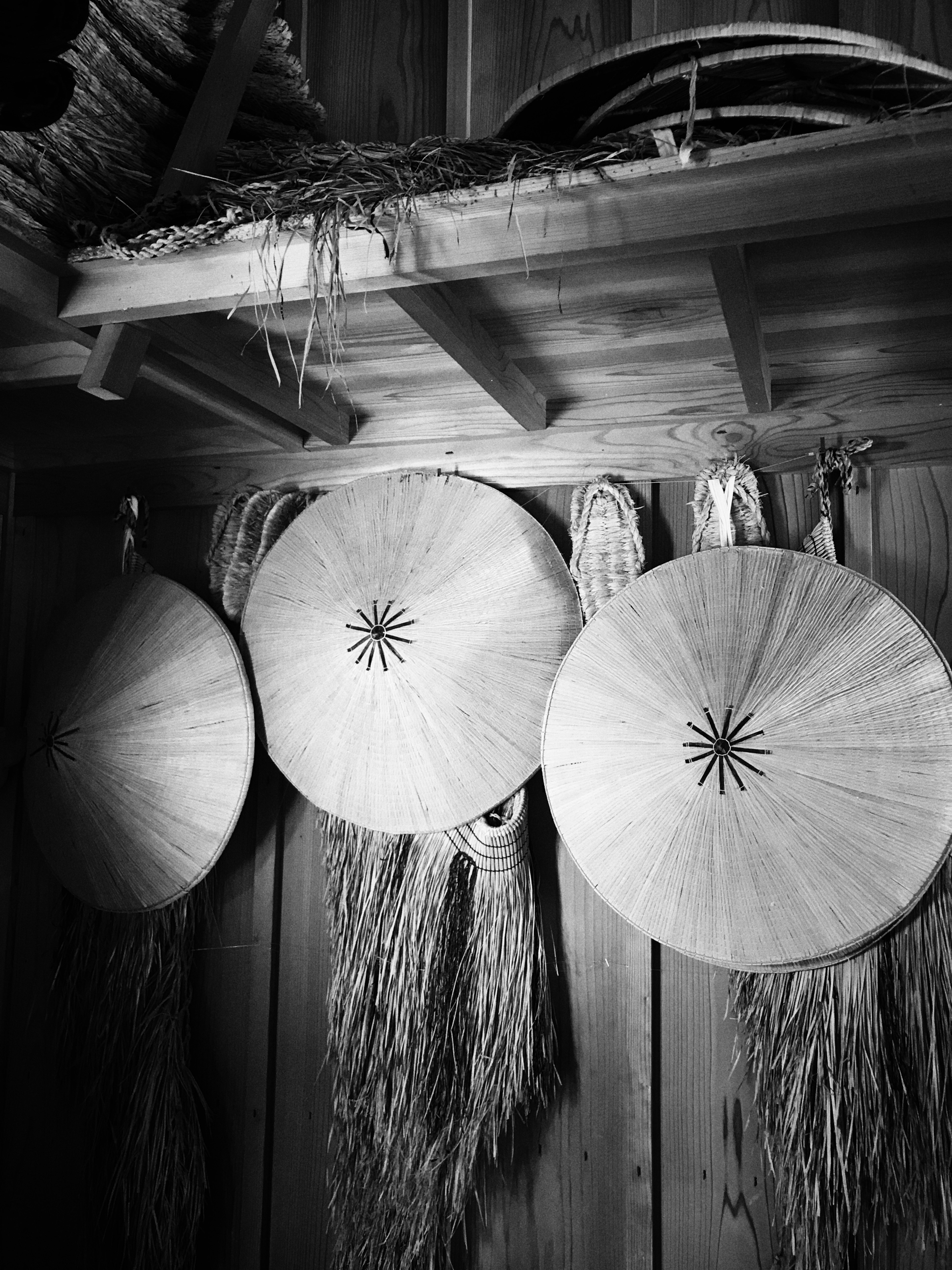 Three round straw hats hanging on a wooden shelf