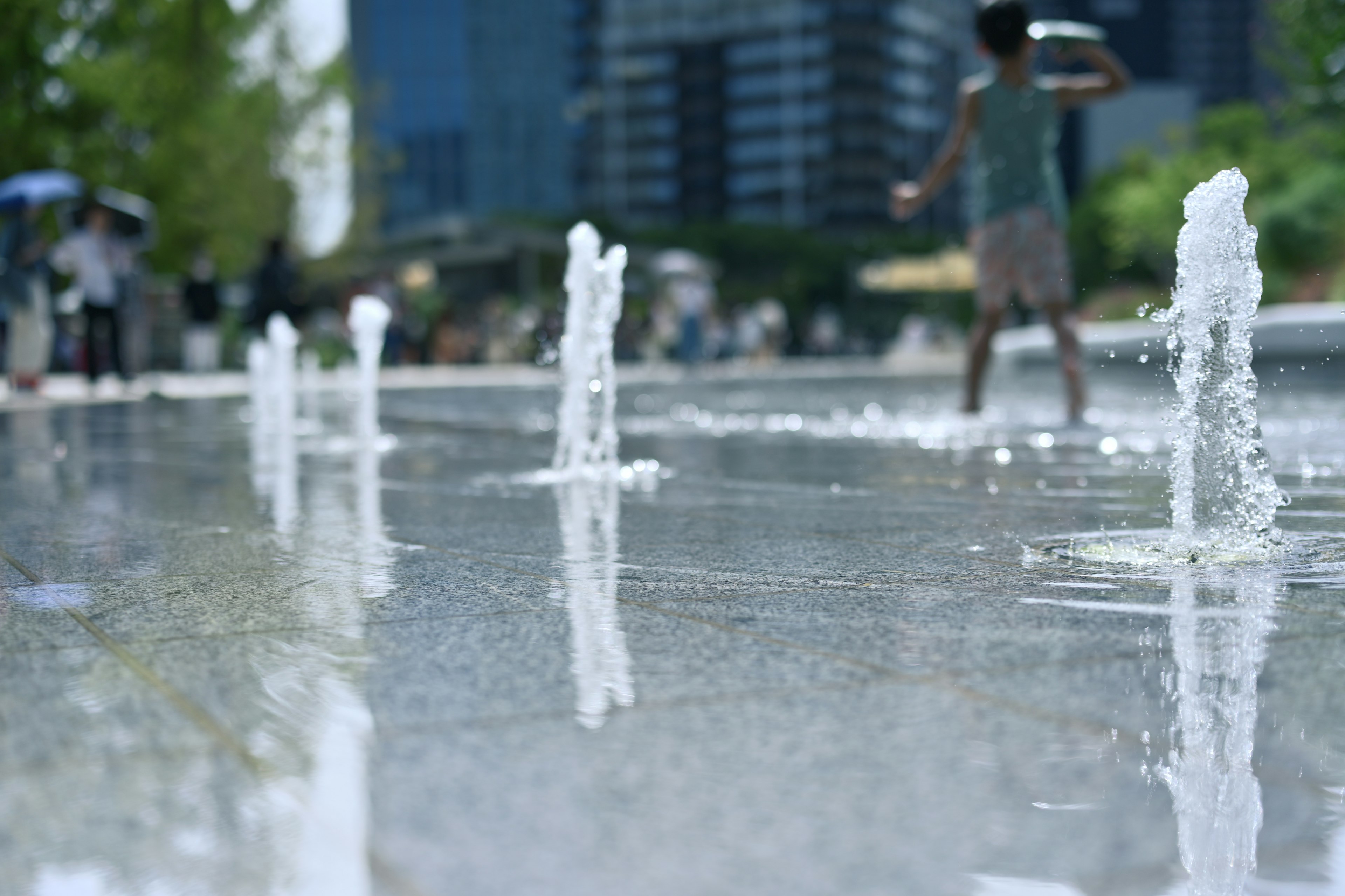 Una escena de parque con fuentes de agua y un niño jugando