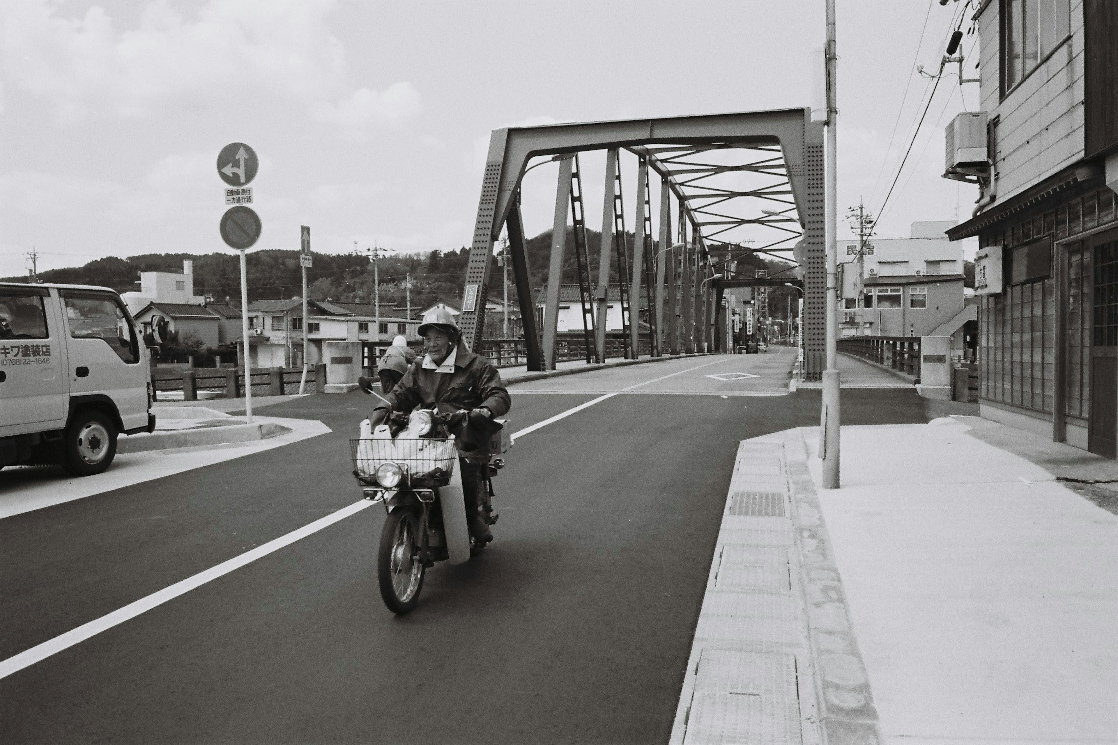 Black and white image of a motorcyclist crossing a bridge