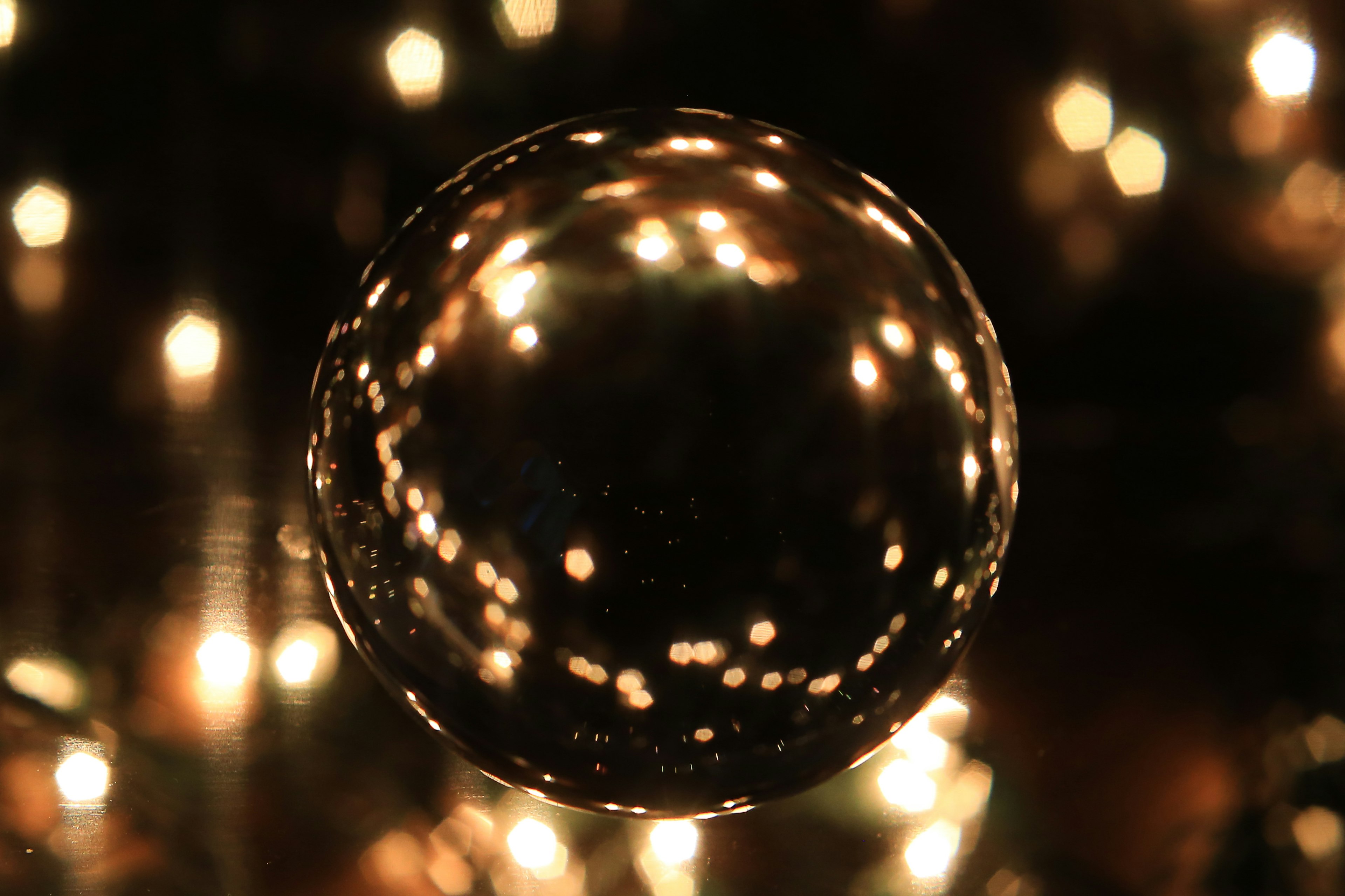 Shiny spherical object reflecting soft lights in a blurred background