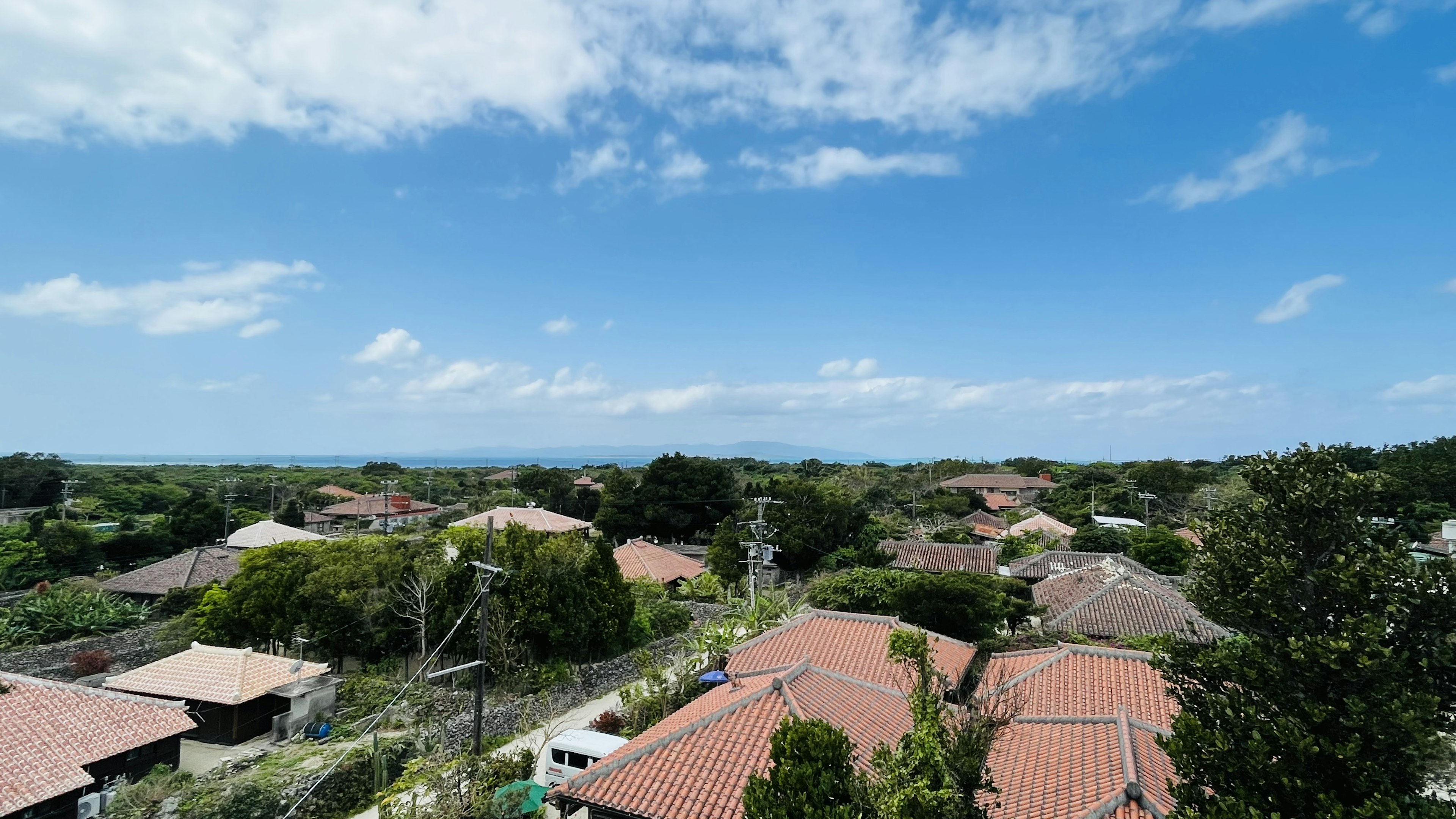 青空と白い雲の下に広がる住宅地の景色屋根の上の赤いタイルの家々と緑の木々が見える