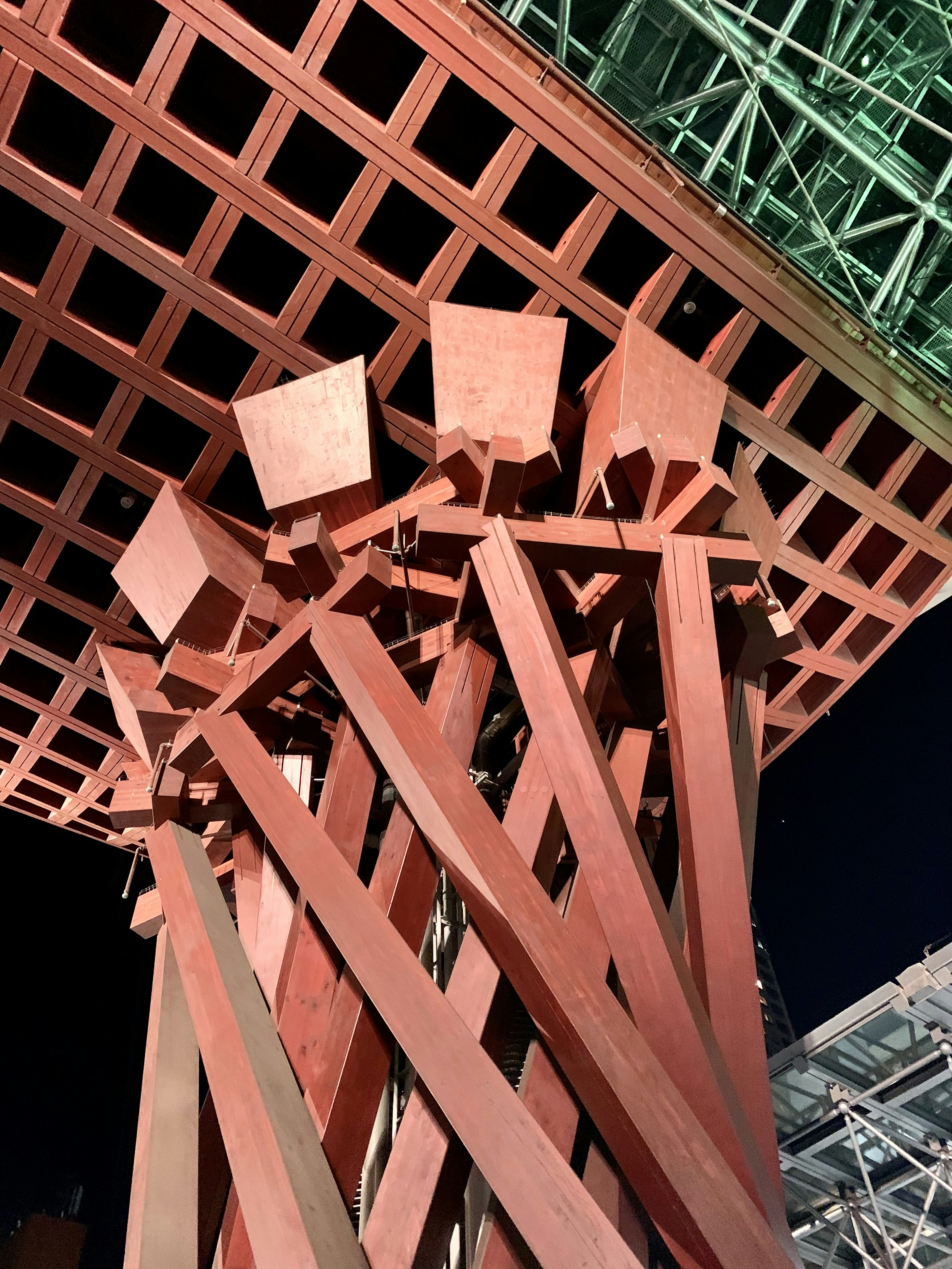 View from below of a structure at night featuring red steel columns and a grid-like ceiling