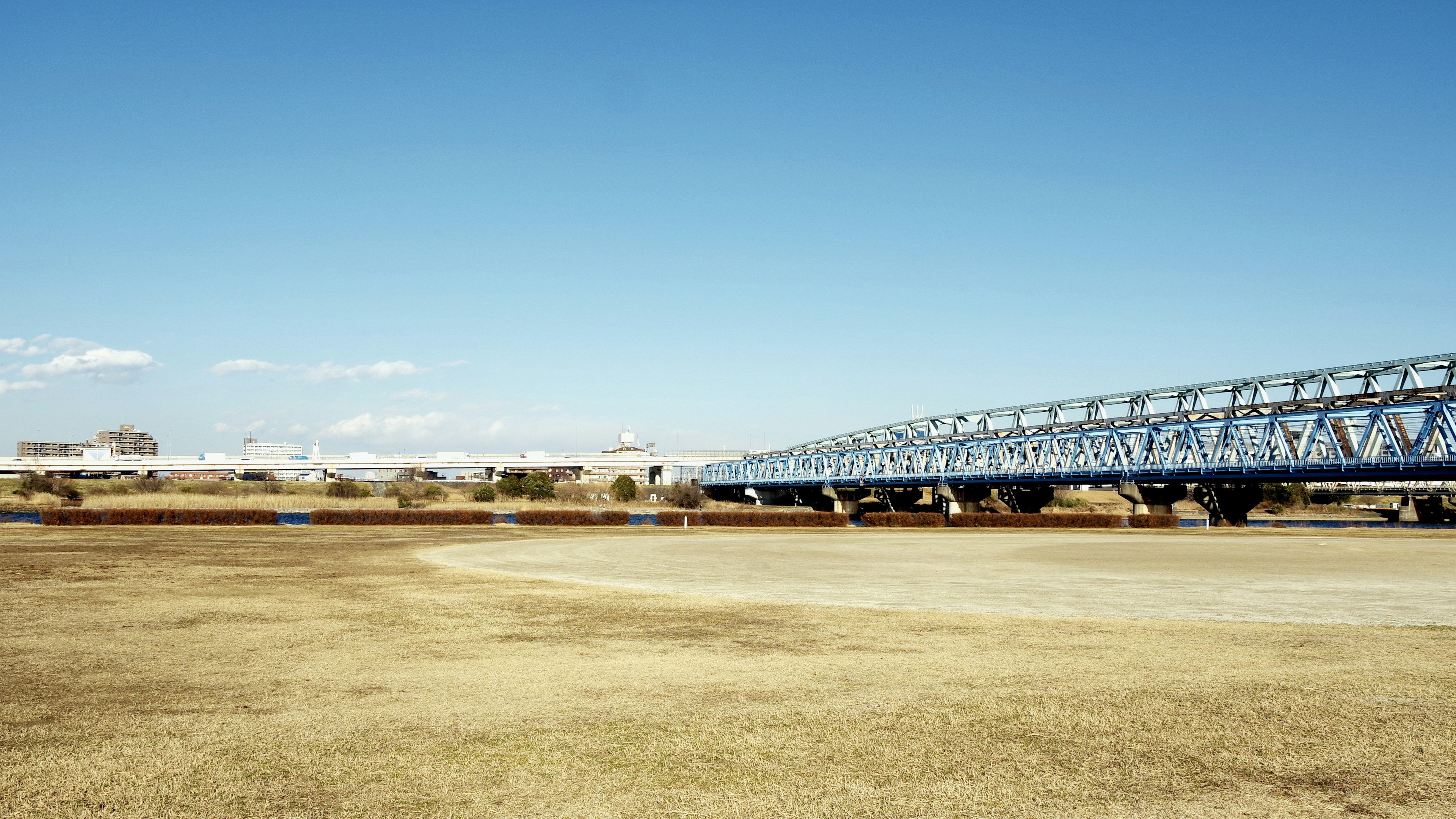 Blue steel bridge under clear sky with dry grassland