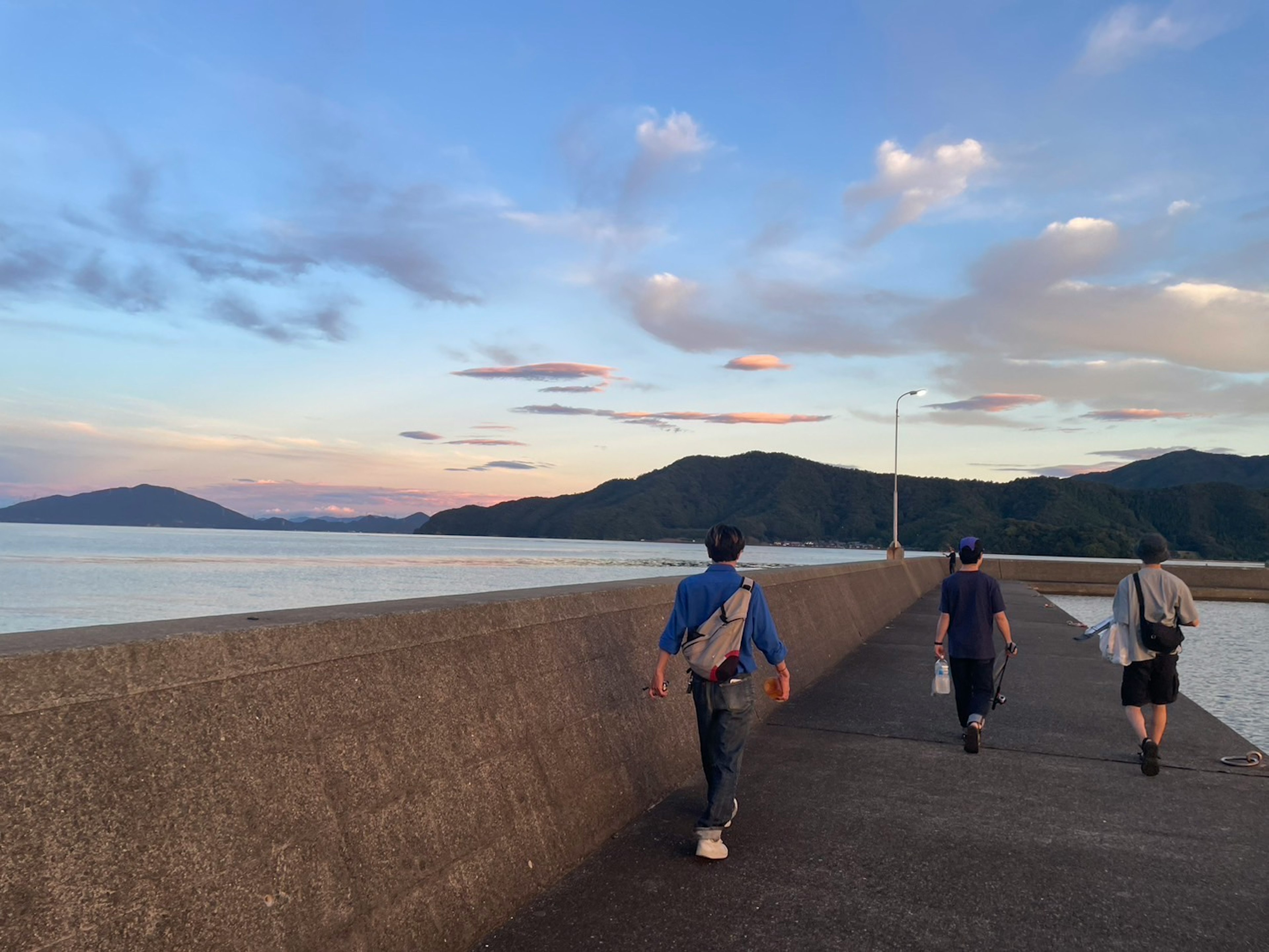 Tres personas caminando por un embarcadero junto al mar con un hermoso cielo al atardecer