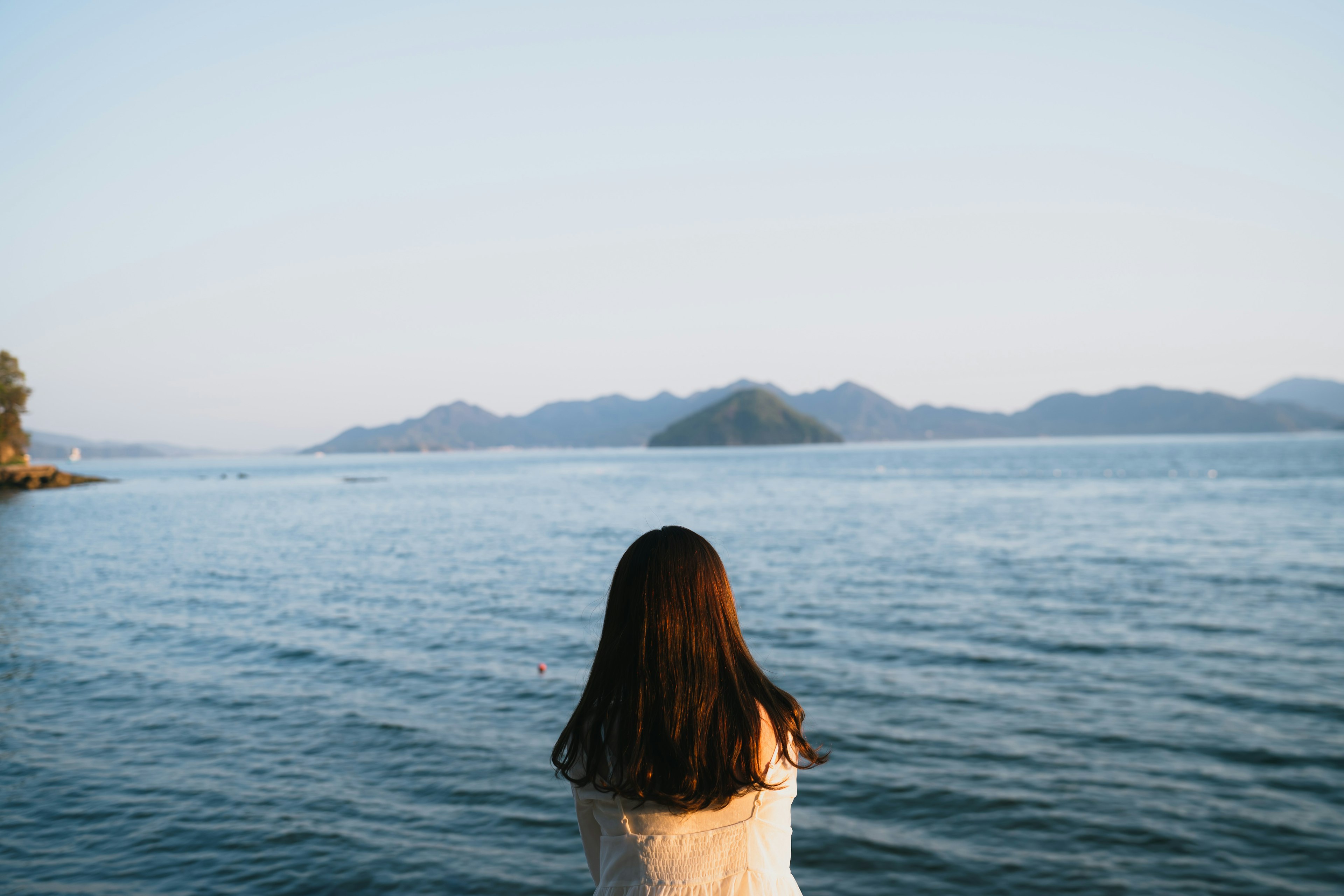 海を見つめる女性の後ろ姿と遠くの山々