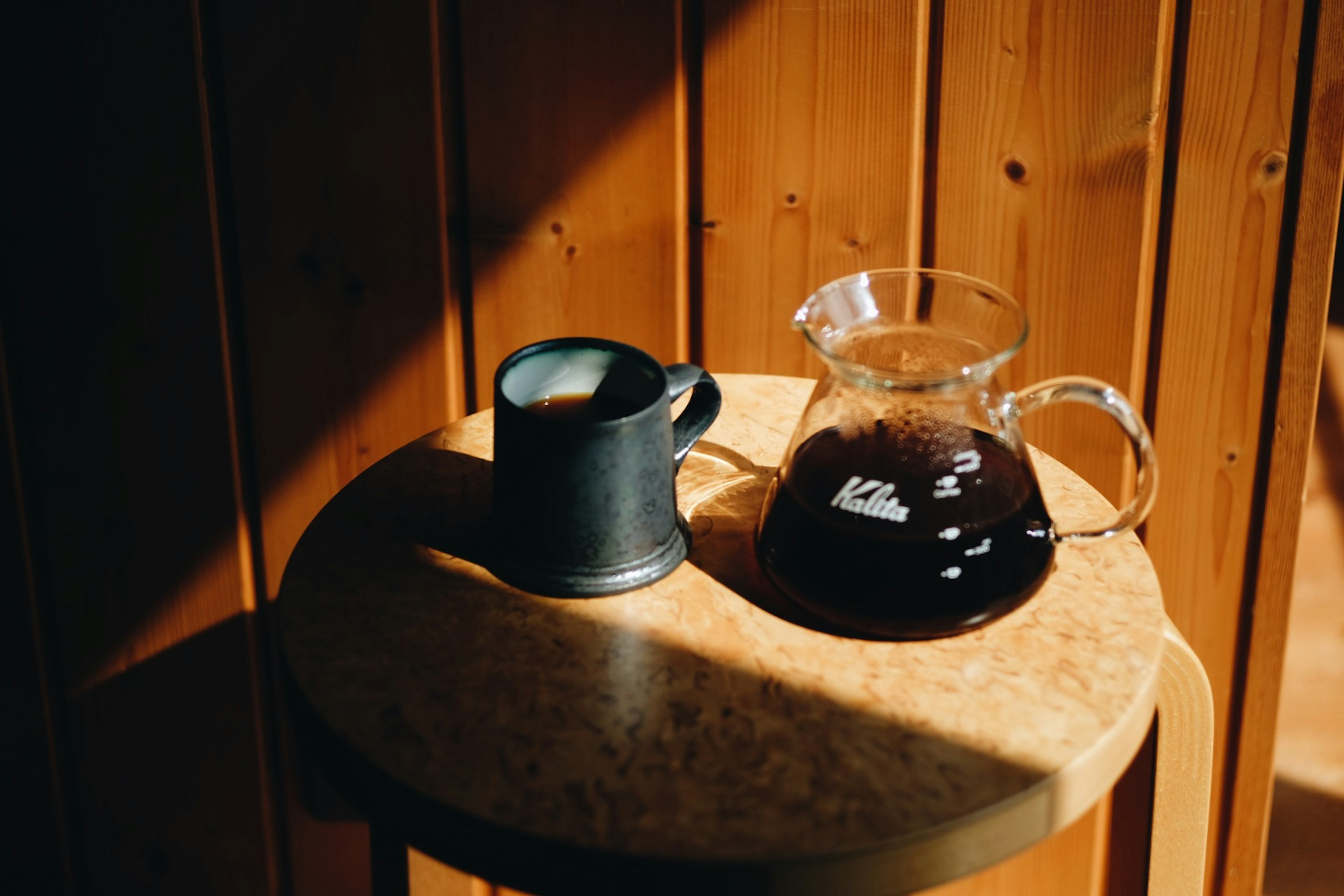 Eine Glaskaffeekaraffe und eine schwarze Tasse auf einem Holztisch