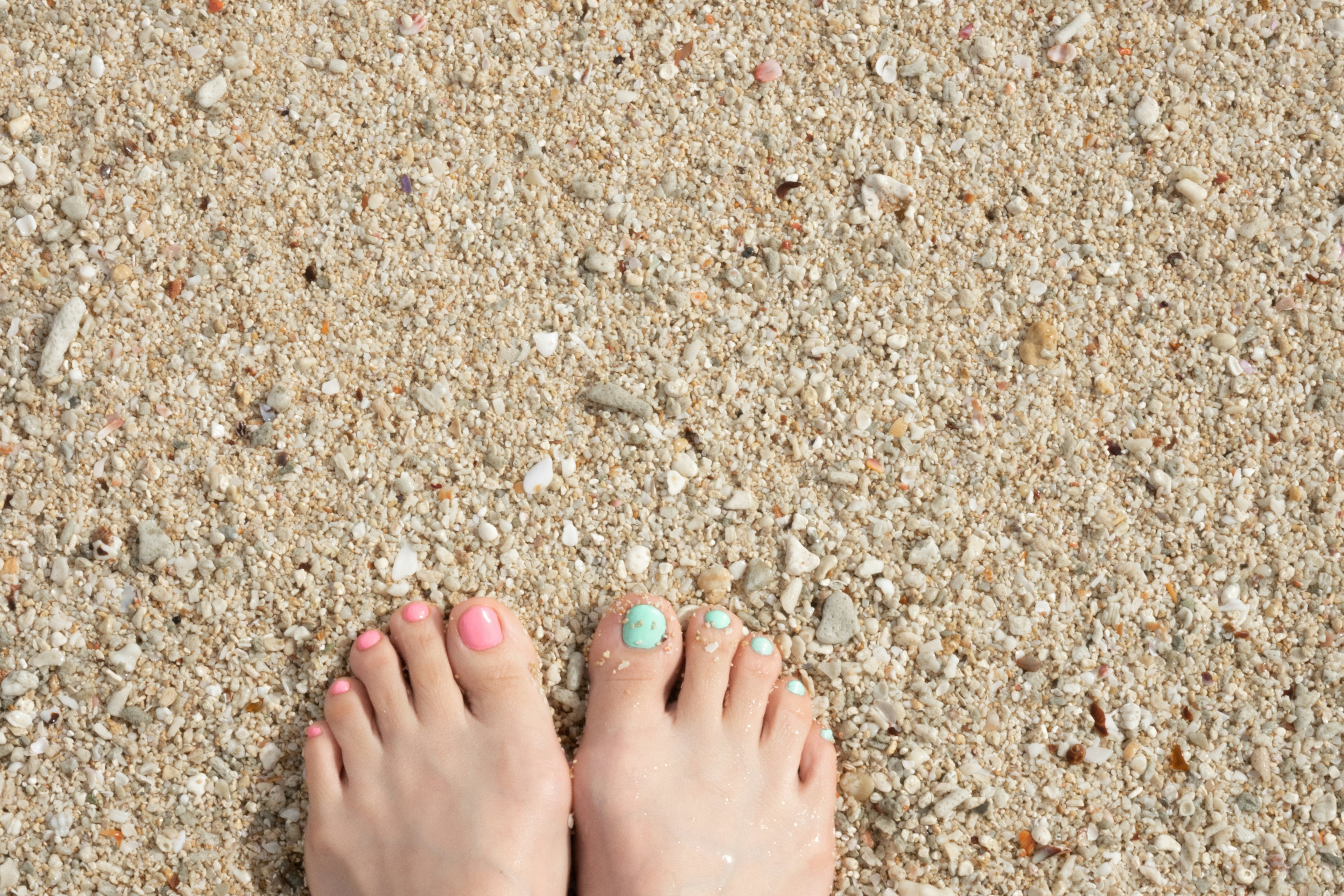 Foto de pies descalzos en una playa de arena con esmalte rosa y azul en los dedos