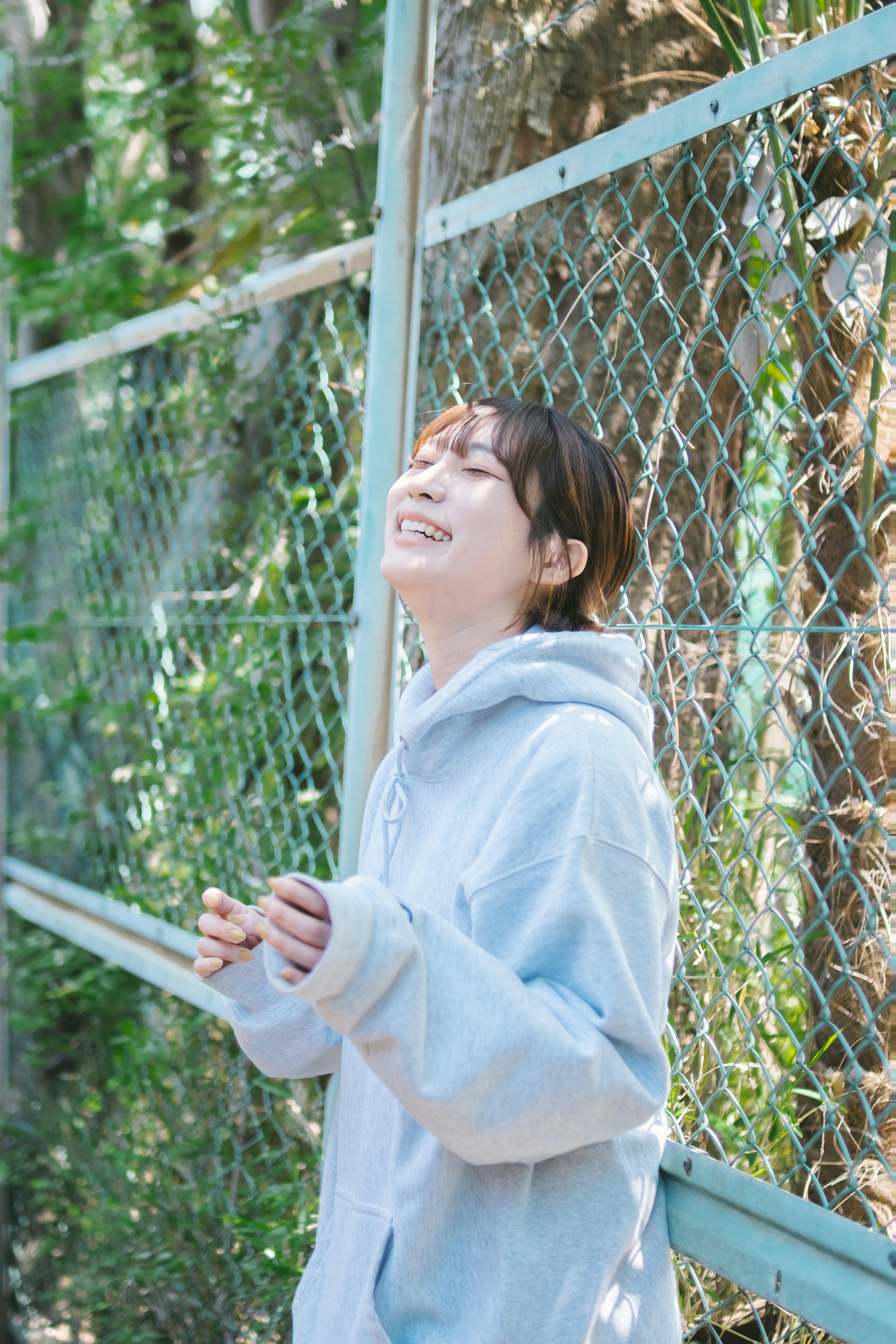 Mujer con sudadera azul sonriendo frente a un árbol