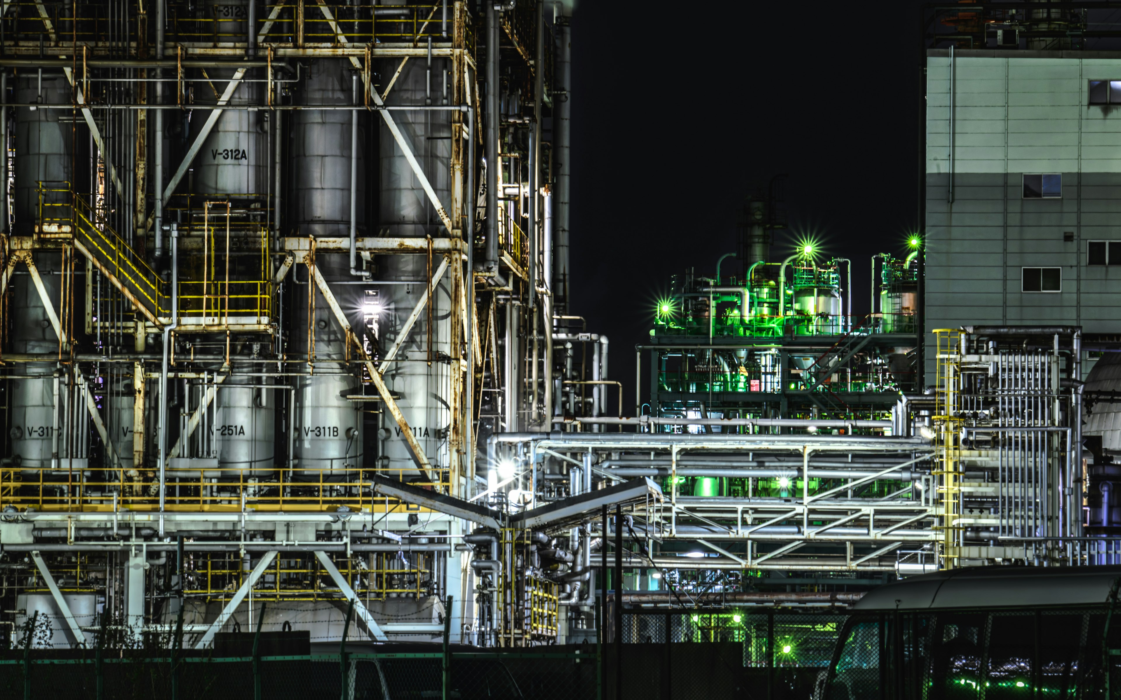 Escena industrial nocturna que muestra grandes tanques de almacenamiento y tuberías iluminadas