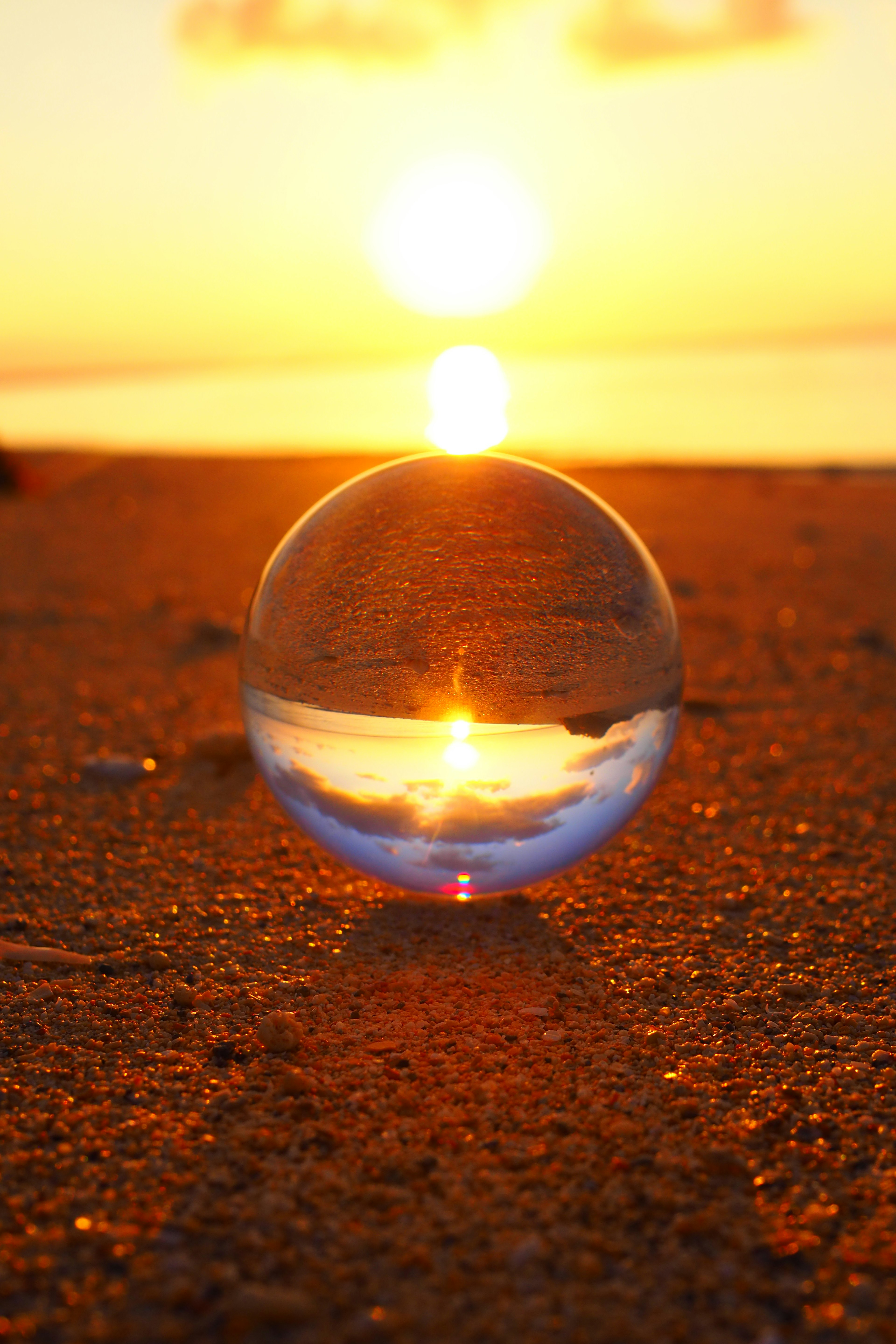 Sfera di vetro trasparente che riflette il tramonto su una spiaggia sabbiosa