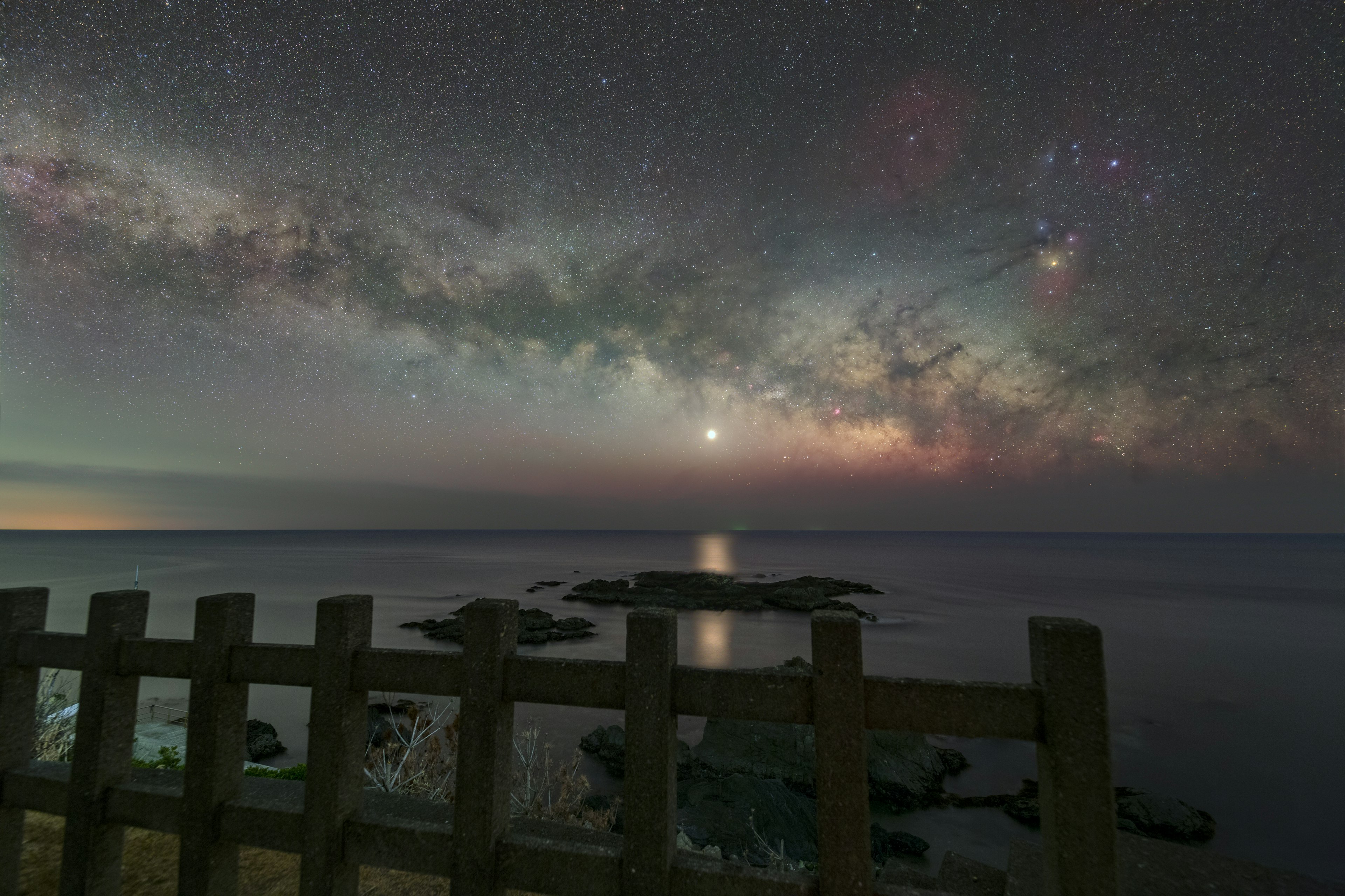 星空の下に広がる海と岩の風景 明るい天体と星雲が見える