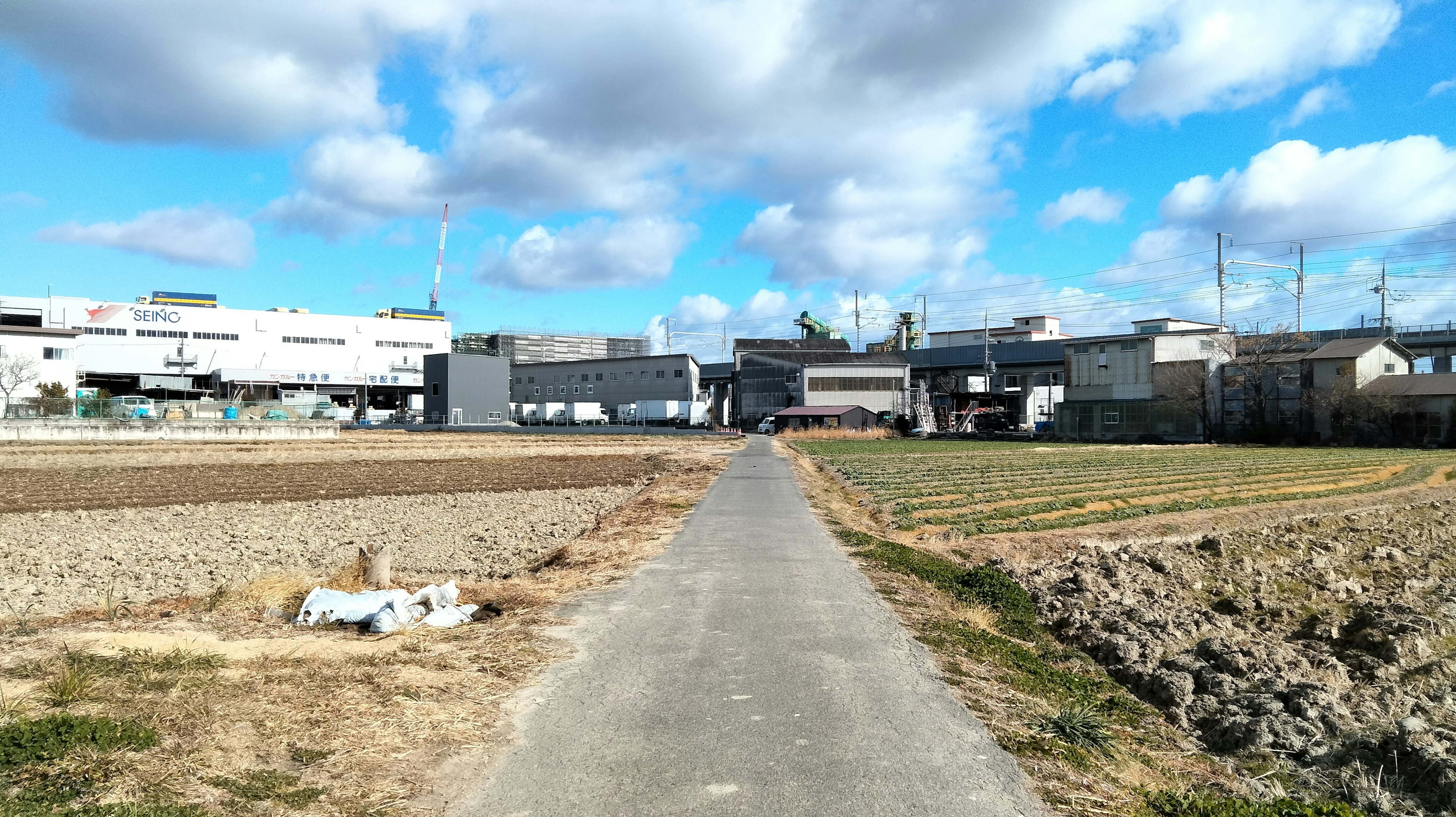 Pathway leading through agricultural land towards industrial buildings