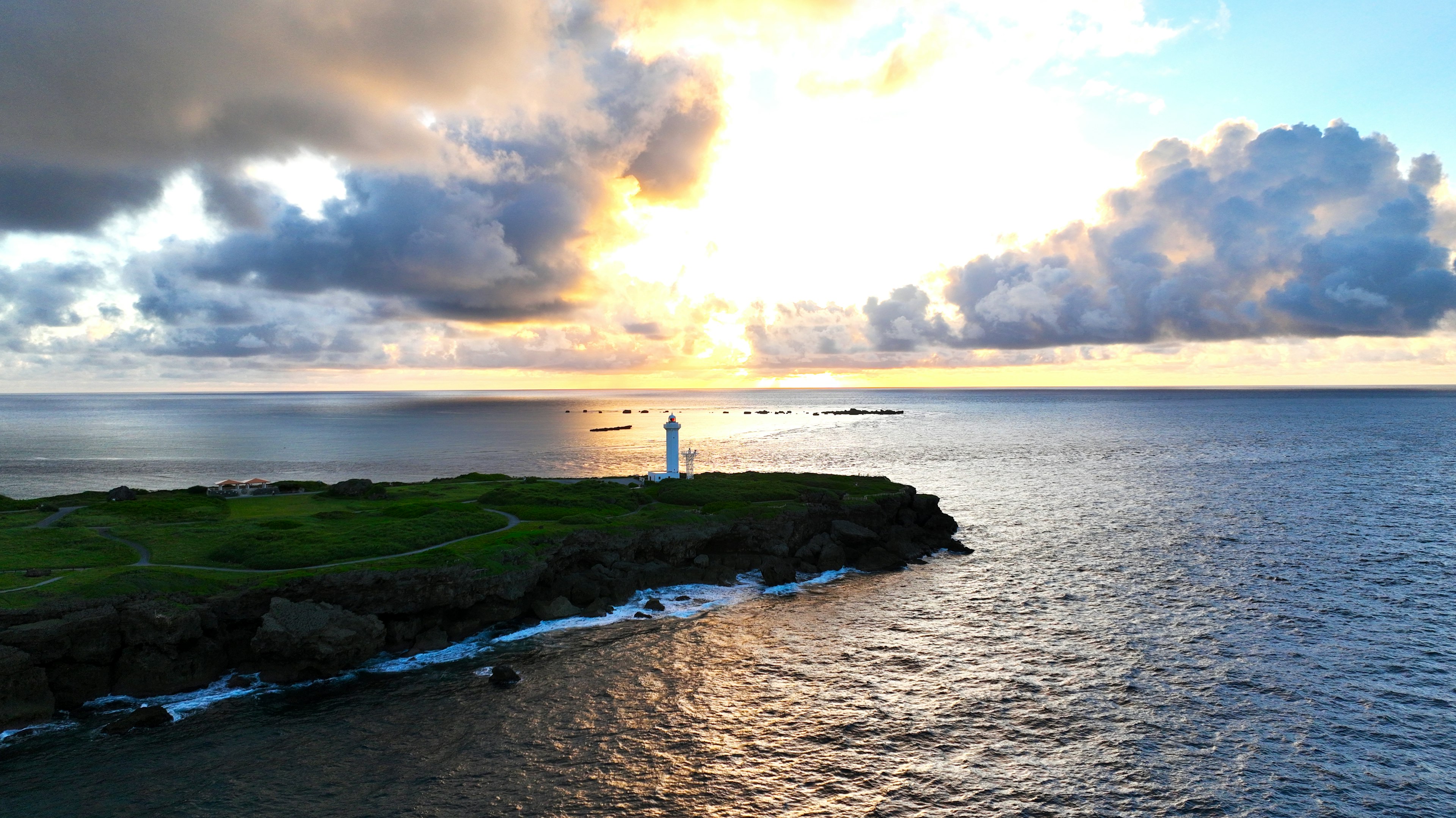 Vista panoramica dell'oceano con un faro al tramonto e nuvole drammatiche