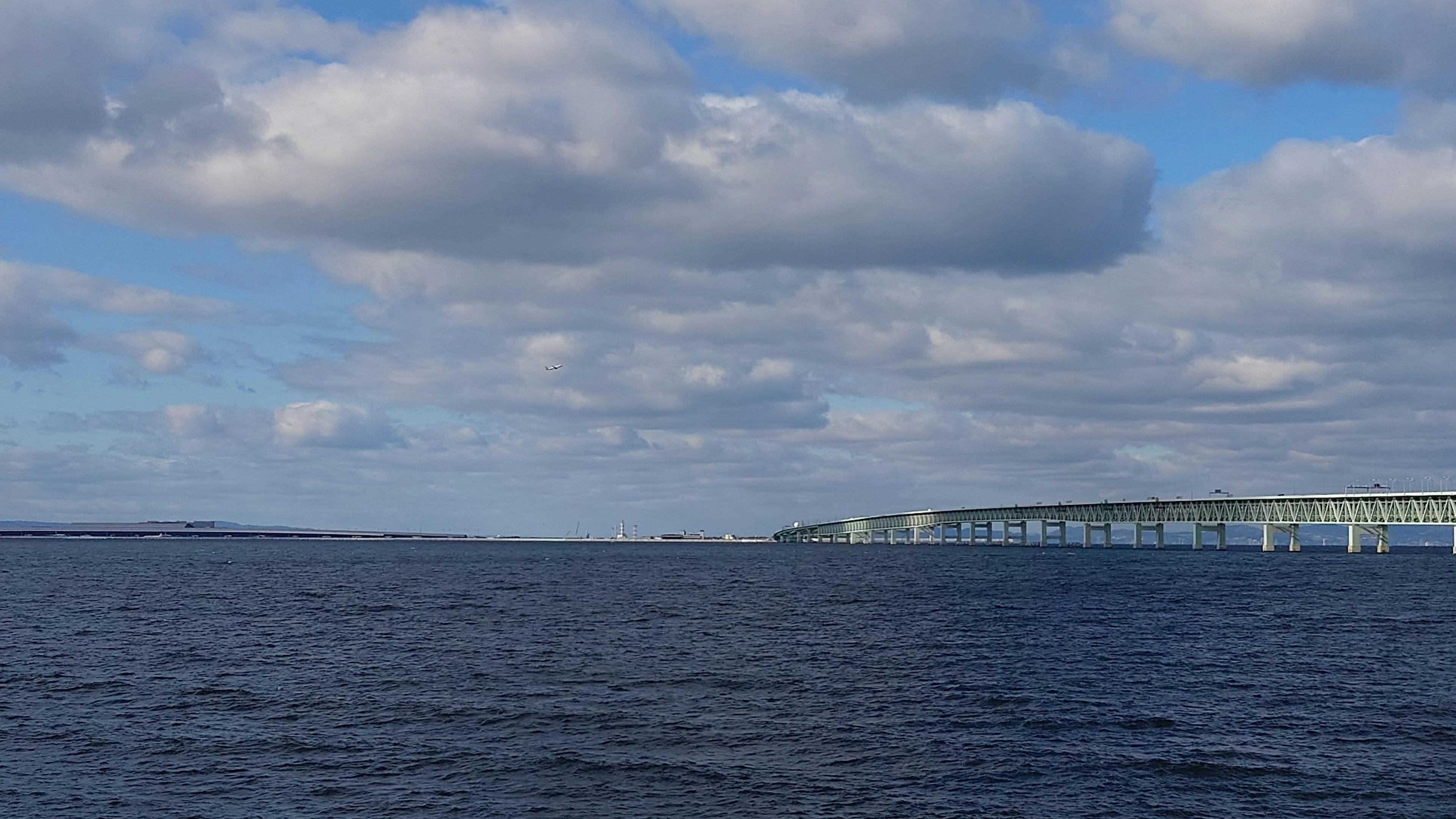 Una vista panoramica di acqua blu con nuvole bianche e un ponte in lontananza