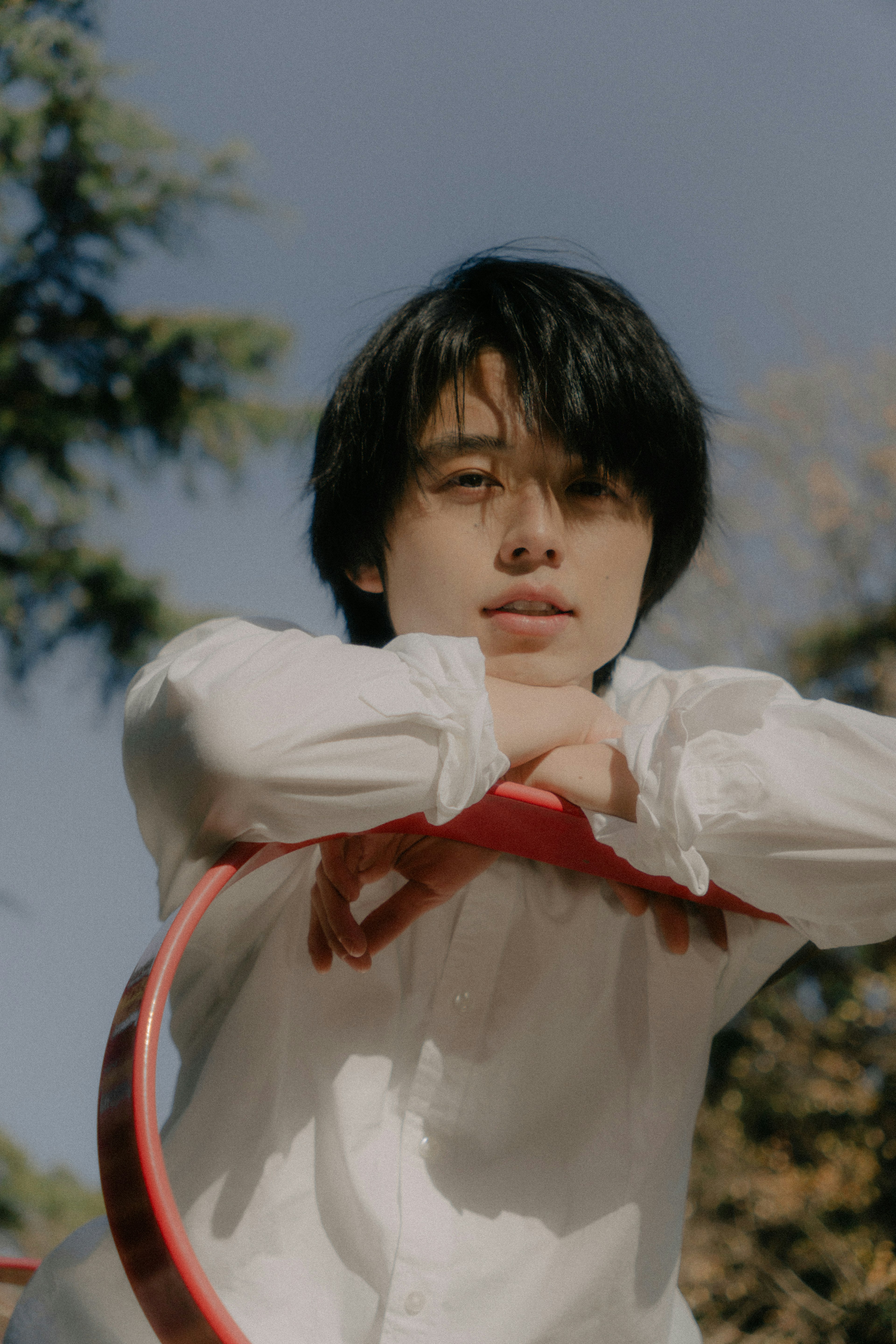 Portrait of a young man holding a red hula hoop in a park