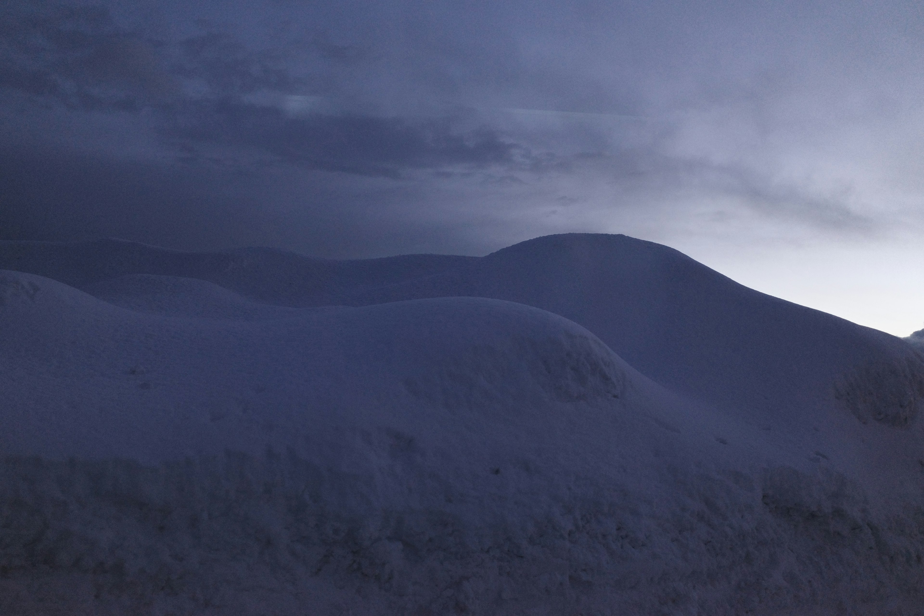 Silhouette de collines enneigées sous un ciel sombre