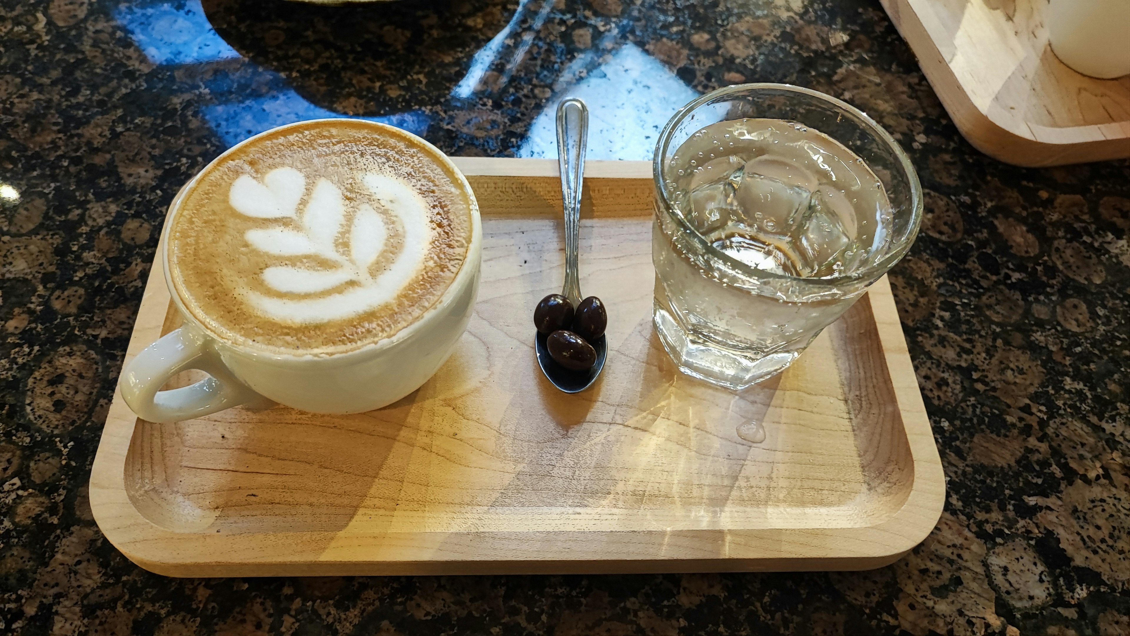 A wooden tray with a coffee cup and a glass of water