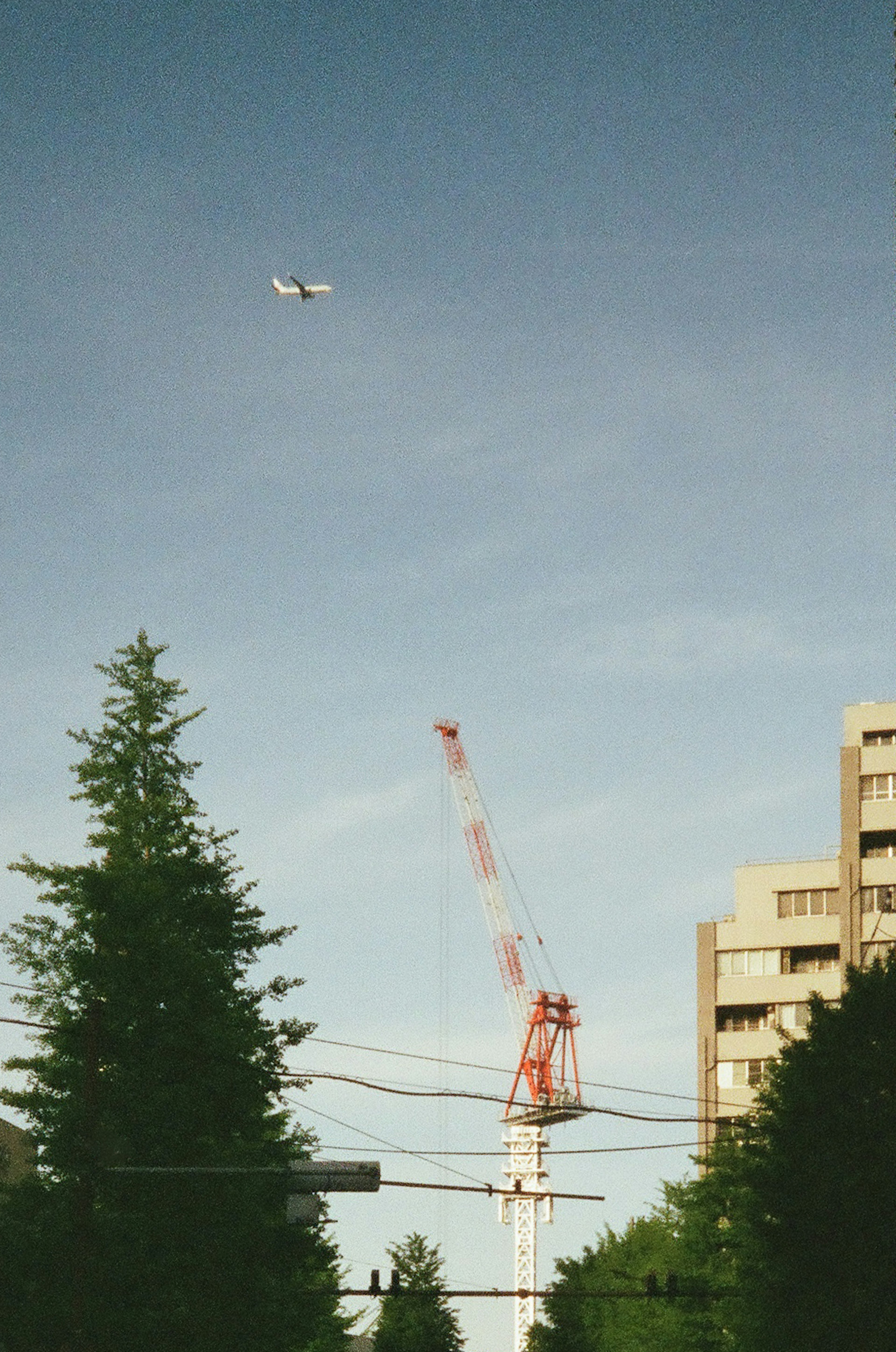 An airplane flying in the blue sky above a red crane and buildings