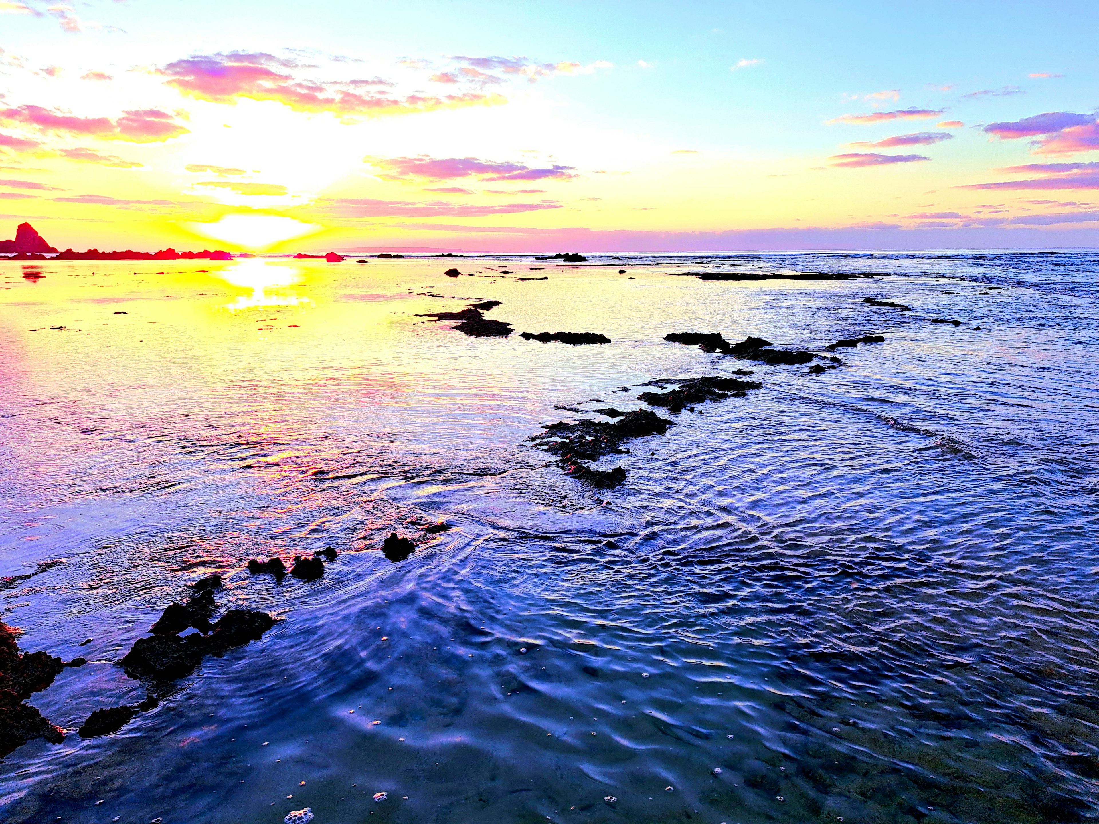 Vista panoramica di un tramonto sull'oceano con una costa rocciosa e onde leggere