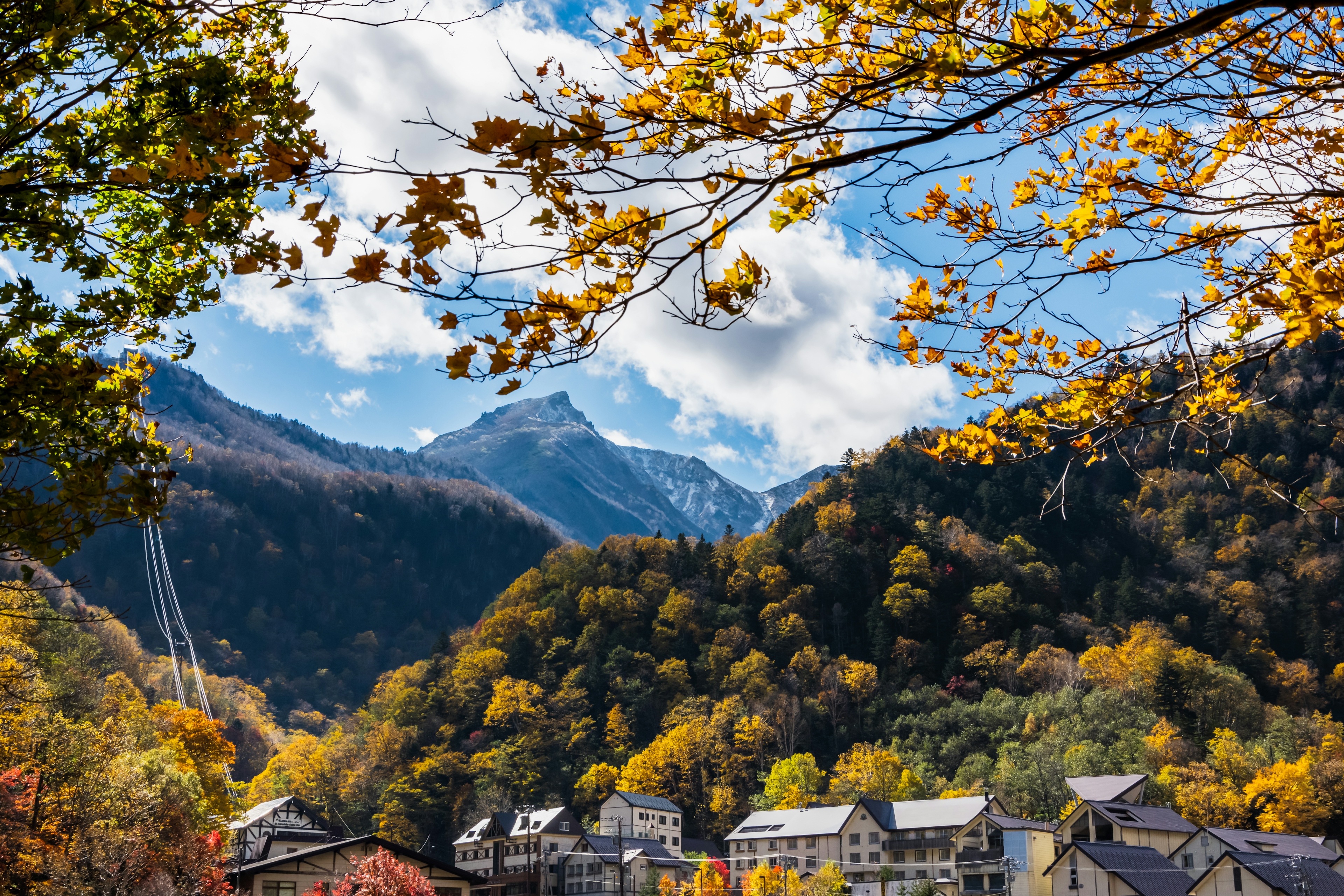 美しい秋の山々と青空が広がる風景 山の麓に小さな家々が点在し 色づいた木々が美しい