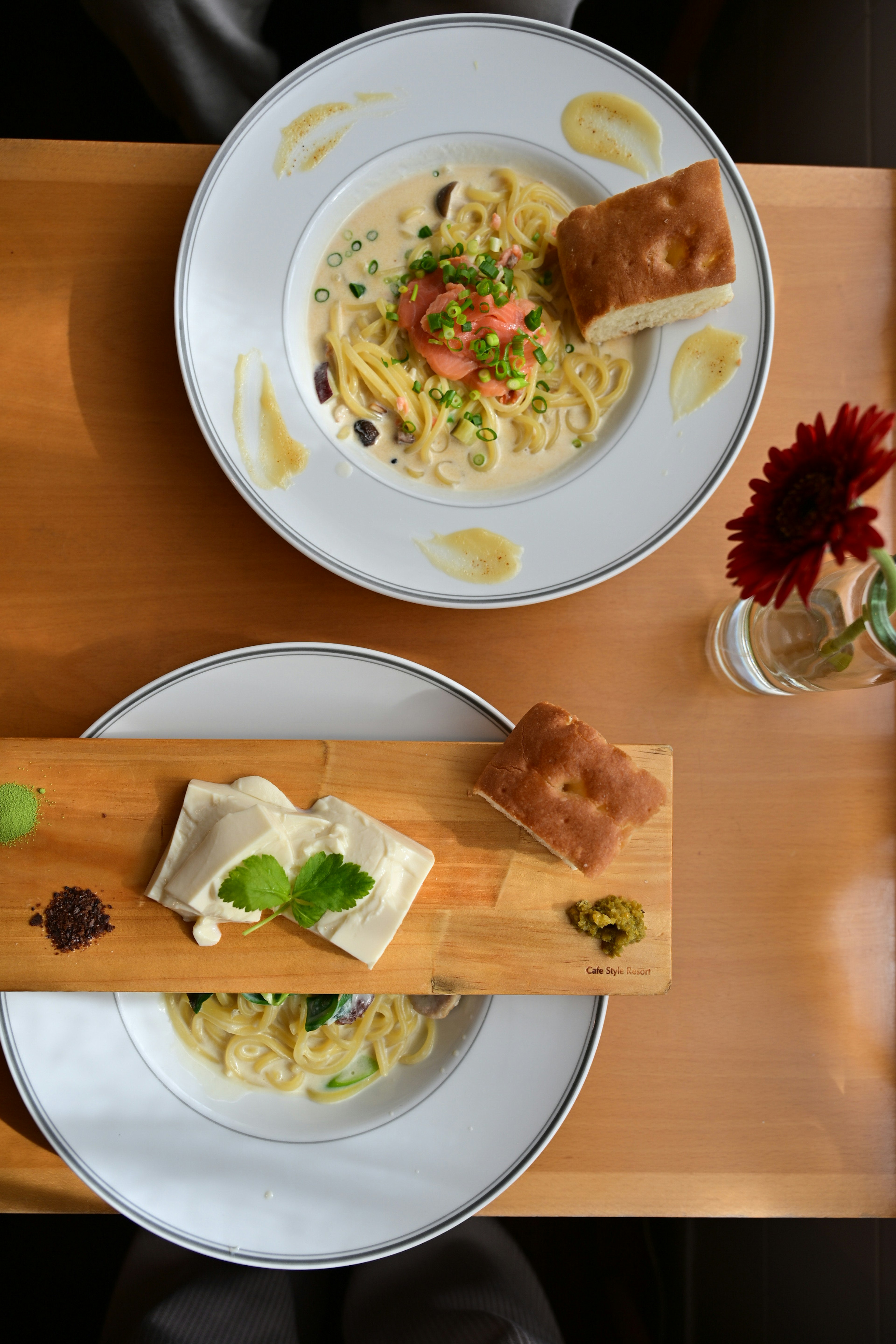 Two plates of pasta with bread served on a wooden board