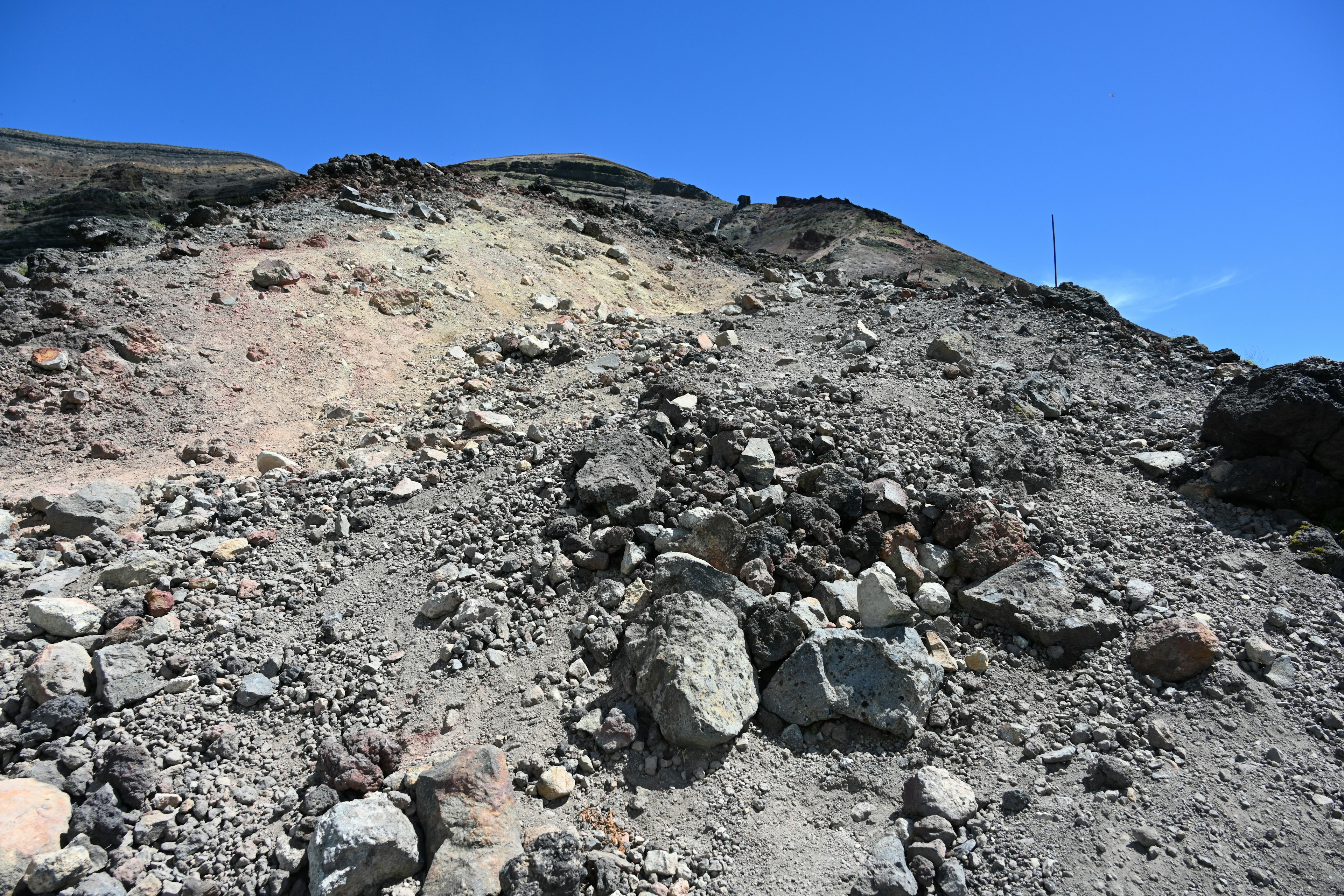 火山の岩や土が積もった斜面の風景青い空が広がる