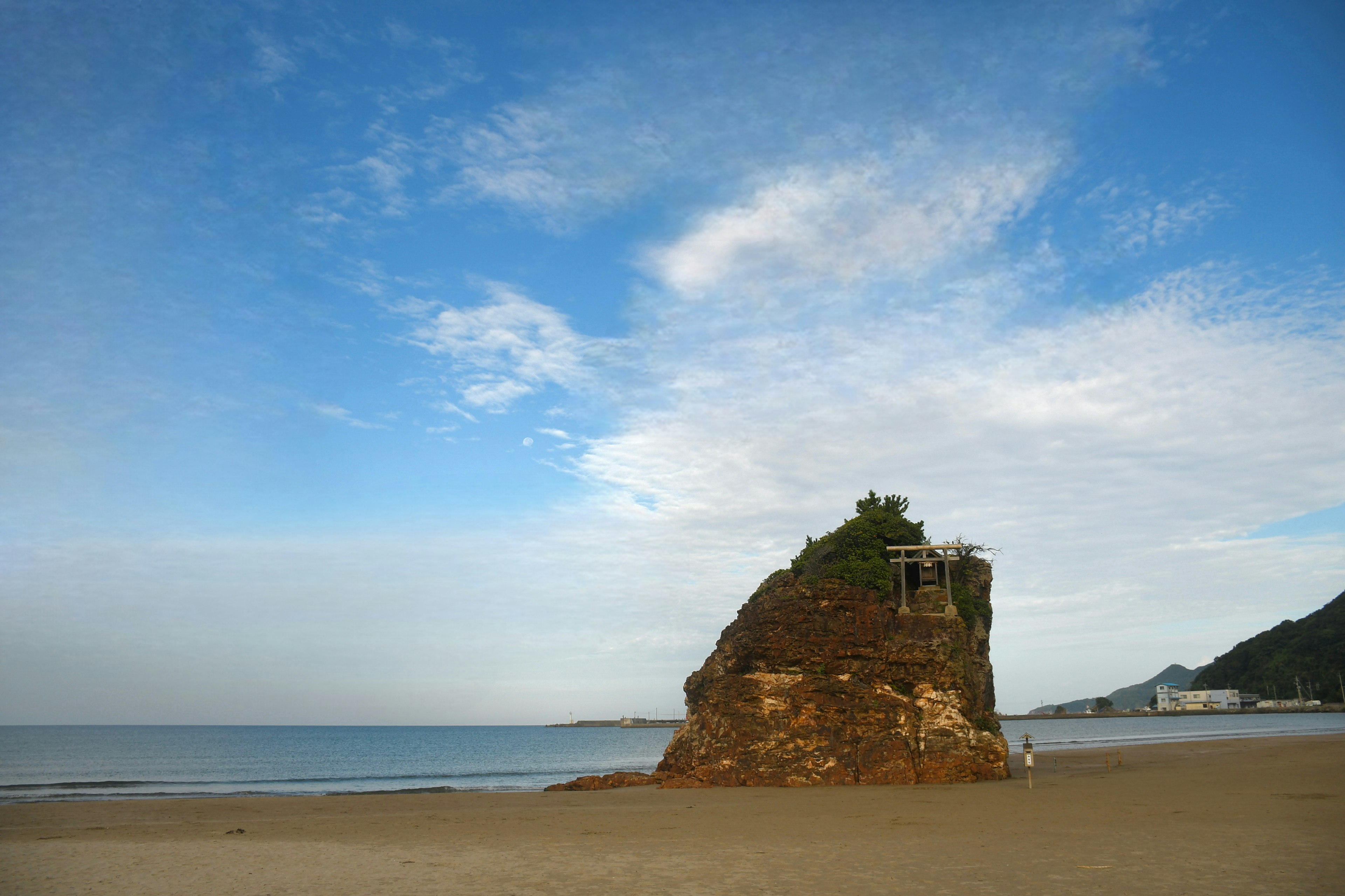 รูปแบบหินที่มีพืชพรรณสีเขียวอยู่บนชายหาดใต้ท้องฟ้าสีฟ้า