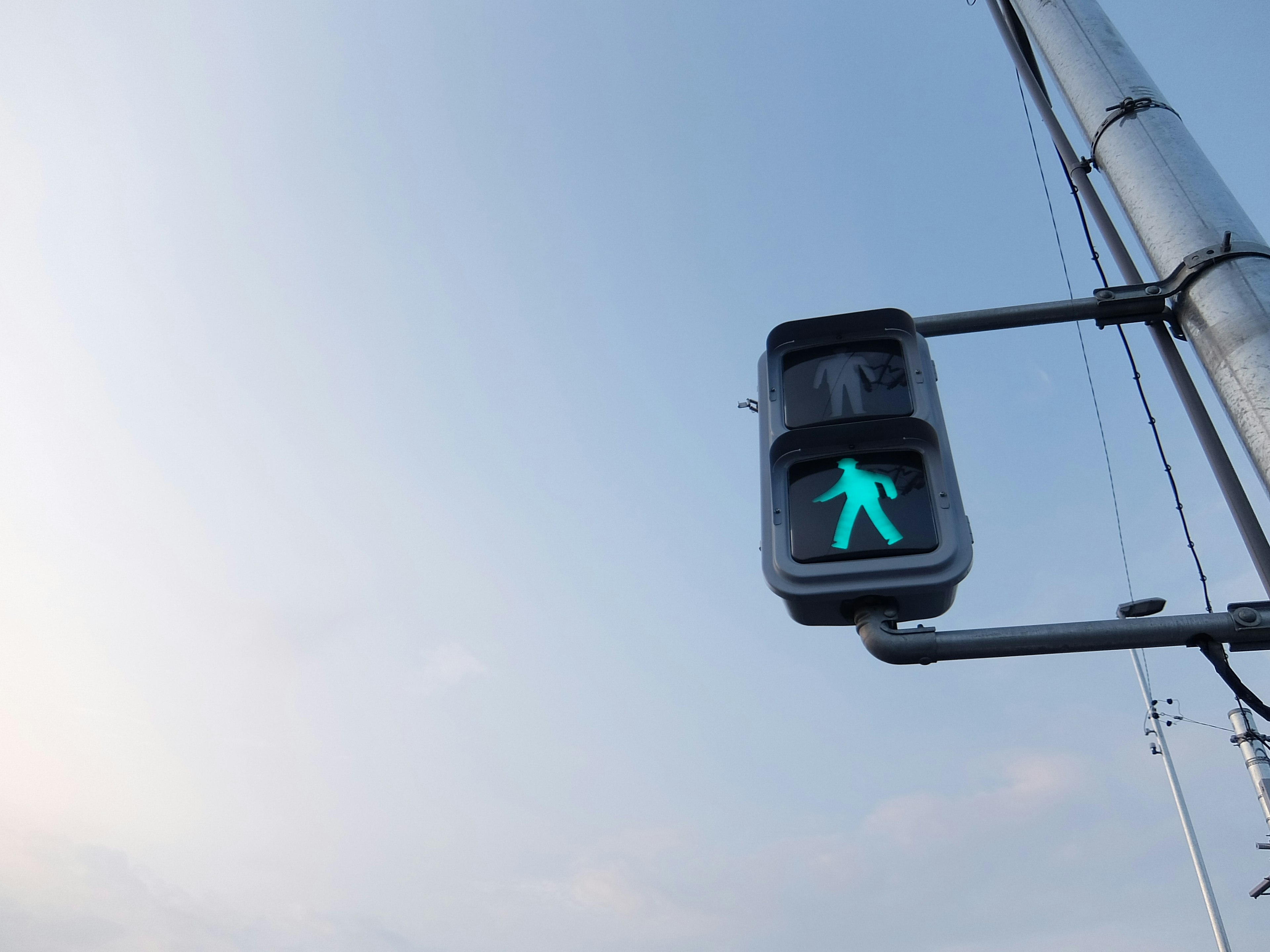 Green pedestrian signal illuminated against a clear sky