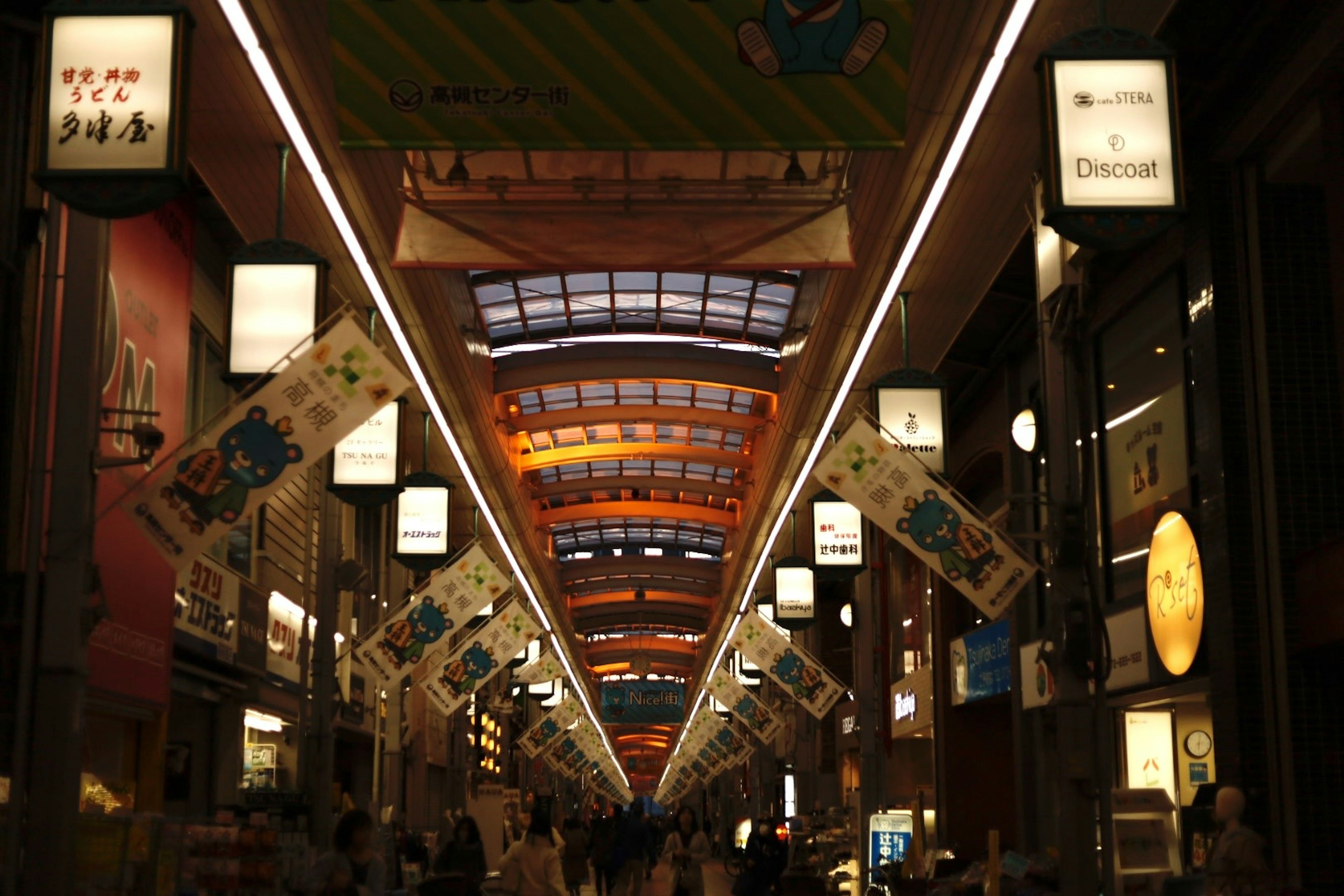 商店街の屋根の下に広がる明るい照明と色とりどりのバナー