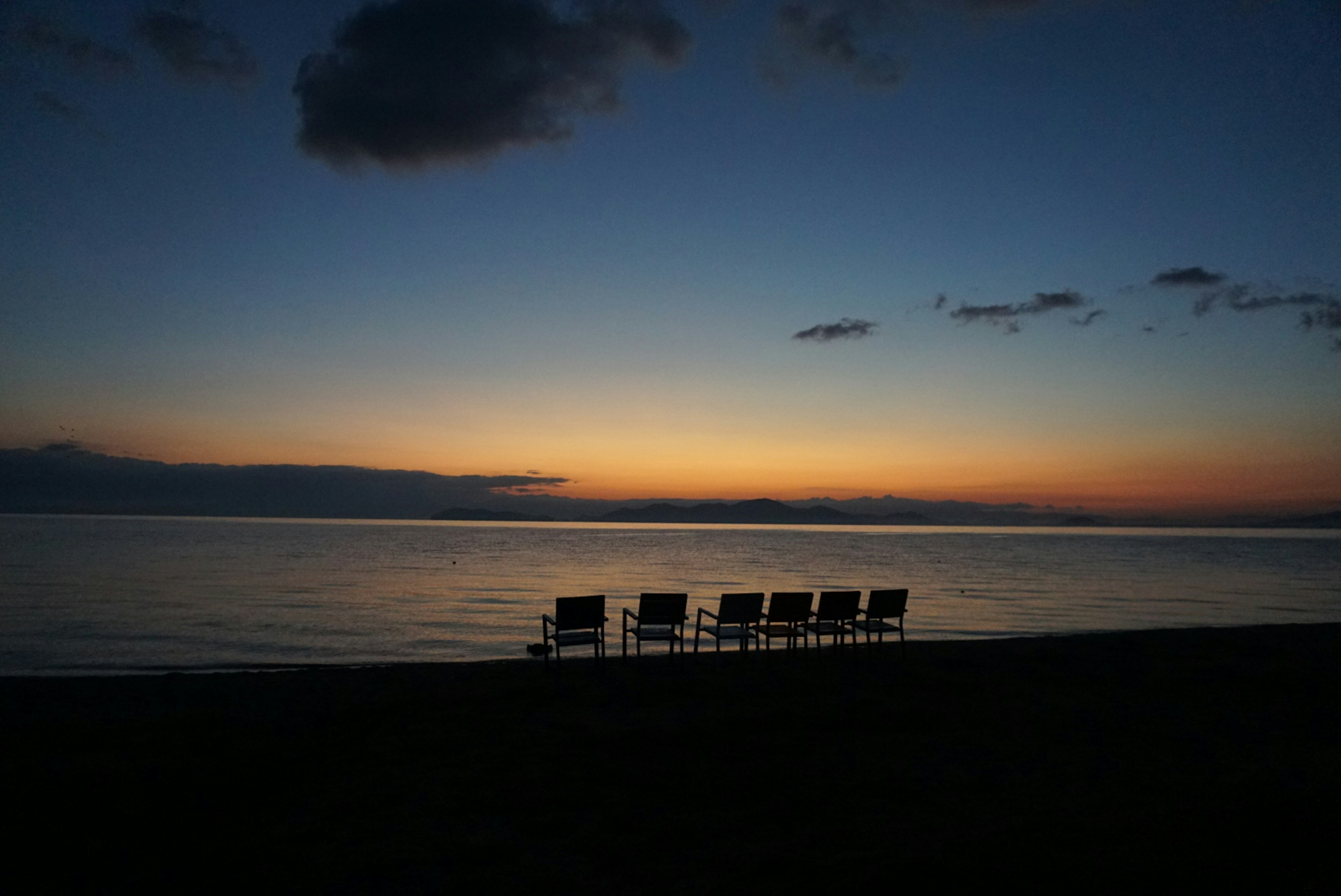 Une scène de plage sereine avec des chaises alignées devant un magnifique coucher de soleil