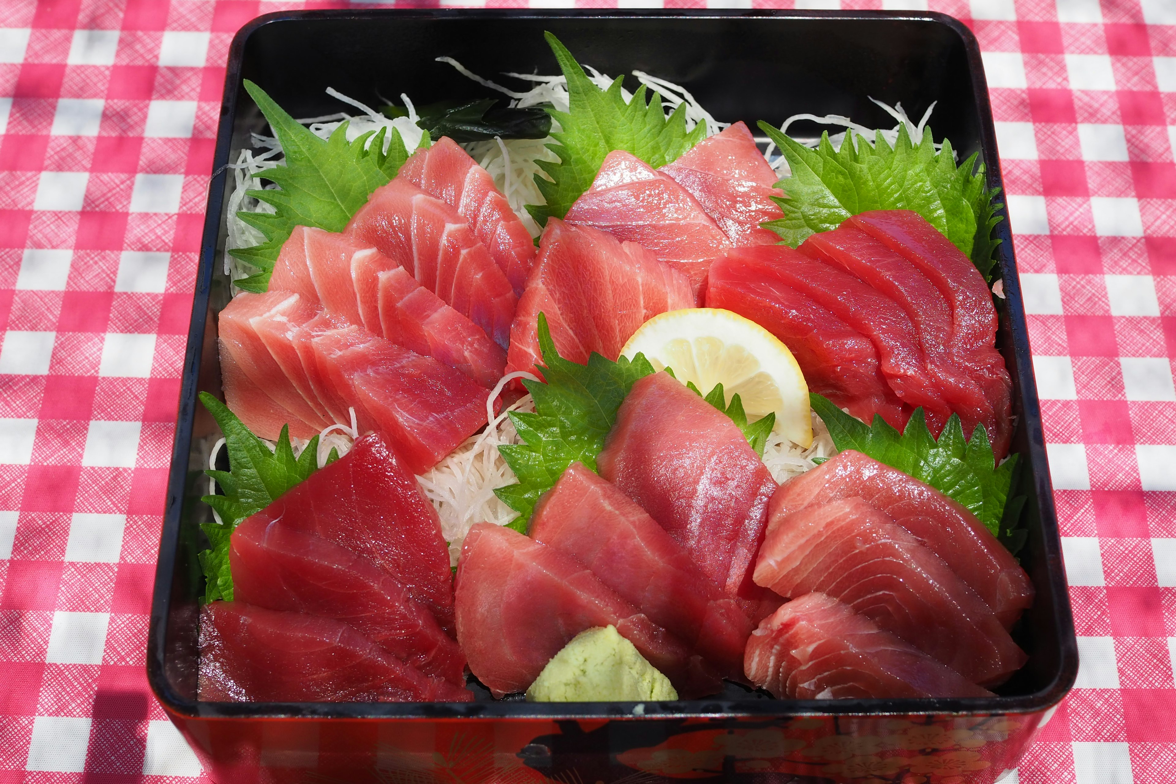 Wadah hitam yang penuh dengan sashimi tuna cerah dihiasi dengan selada dan lemon