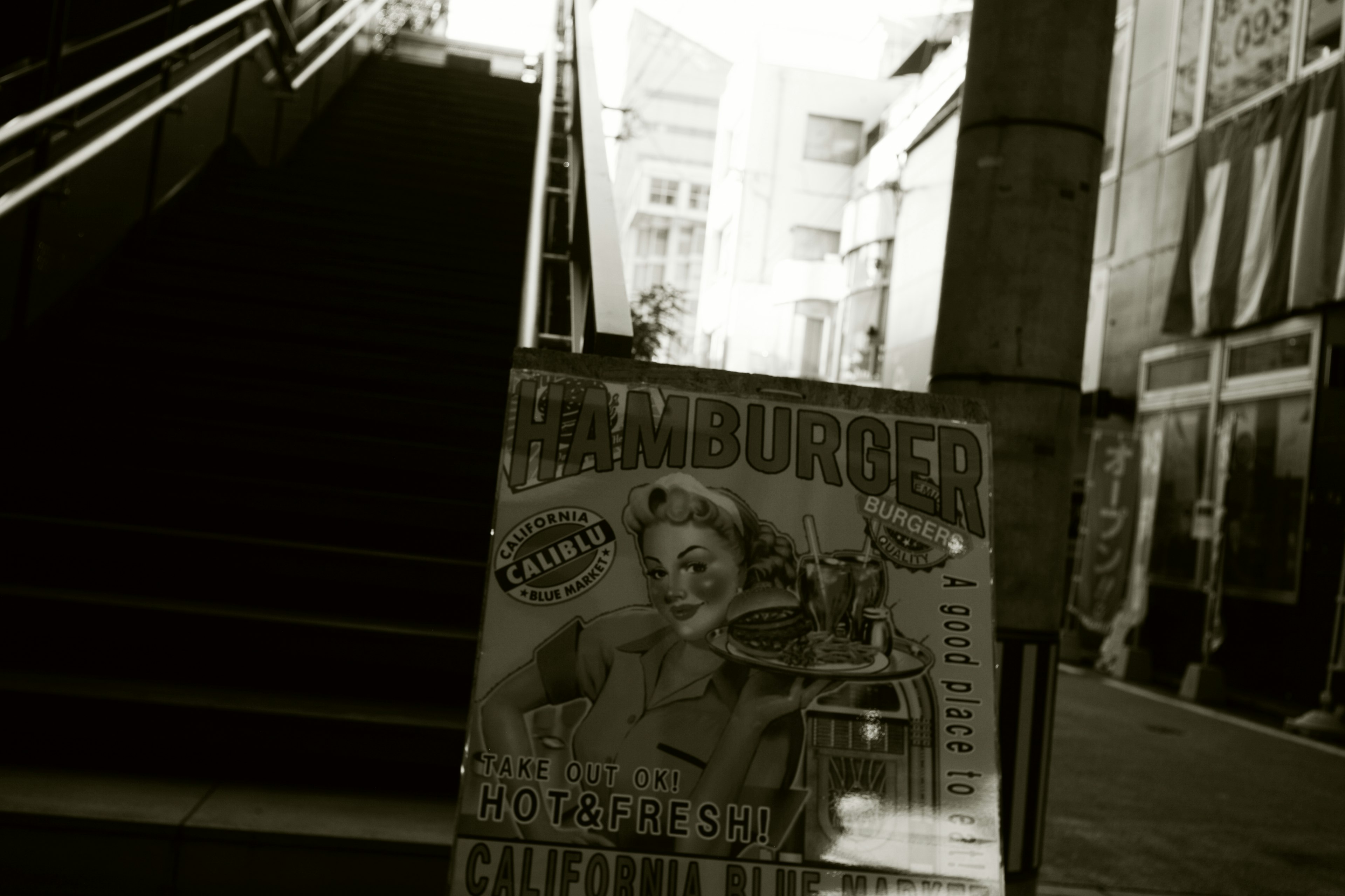 Black and white hamburger poster in front of stairs with surrounding buildings