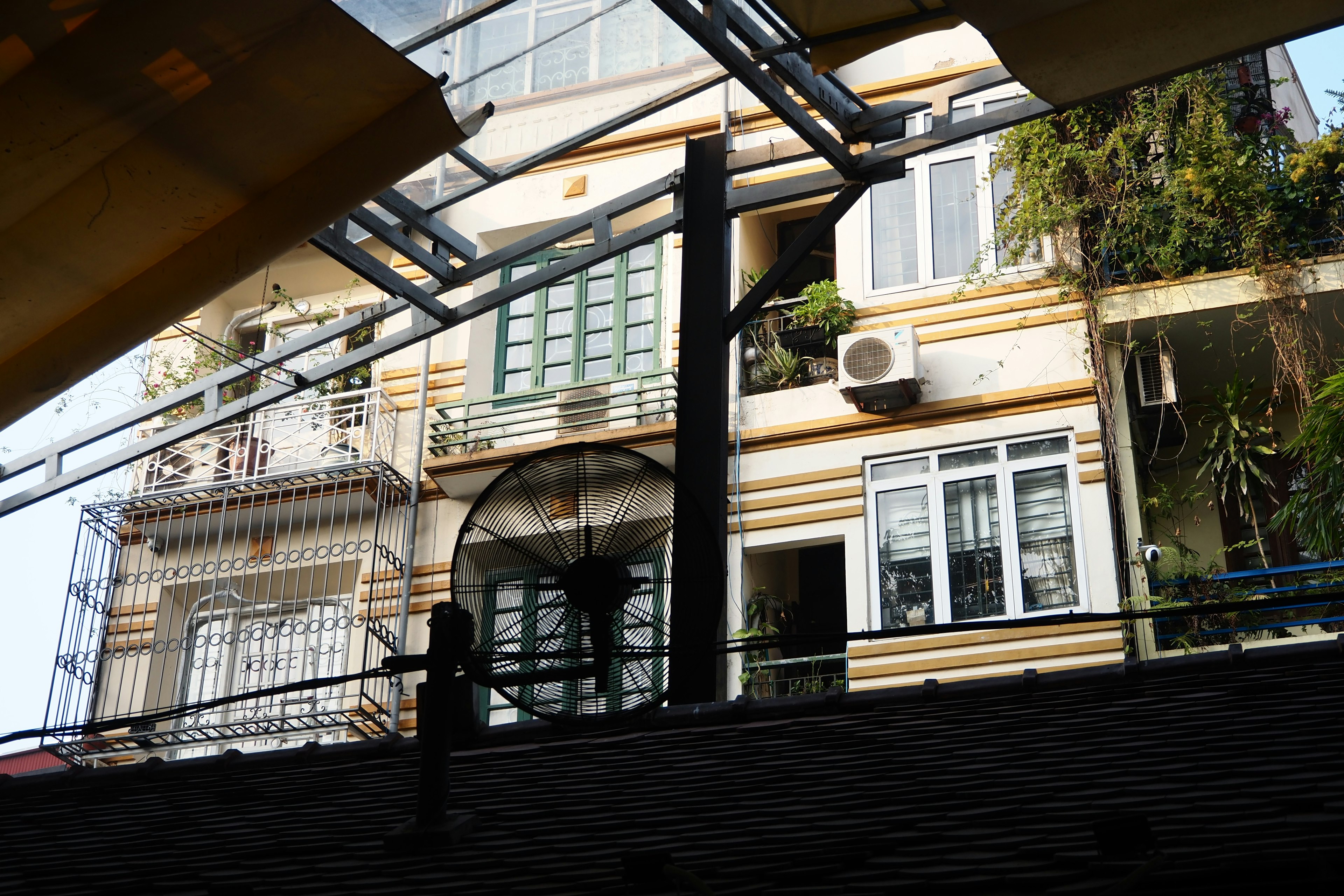 Blick aus einem Fenster auf die Fassade eines Gebäudes mit grünen Pflanzen und Klimaanlagen