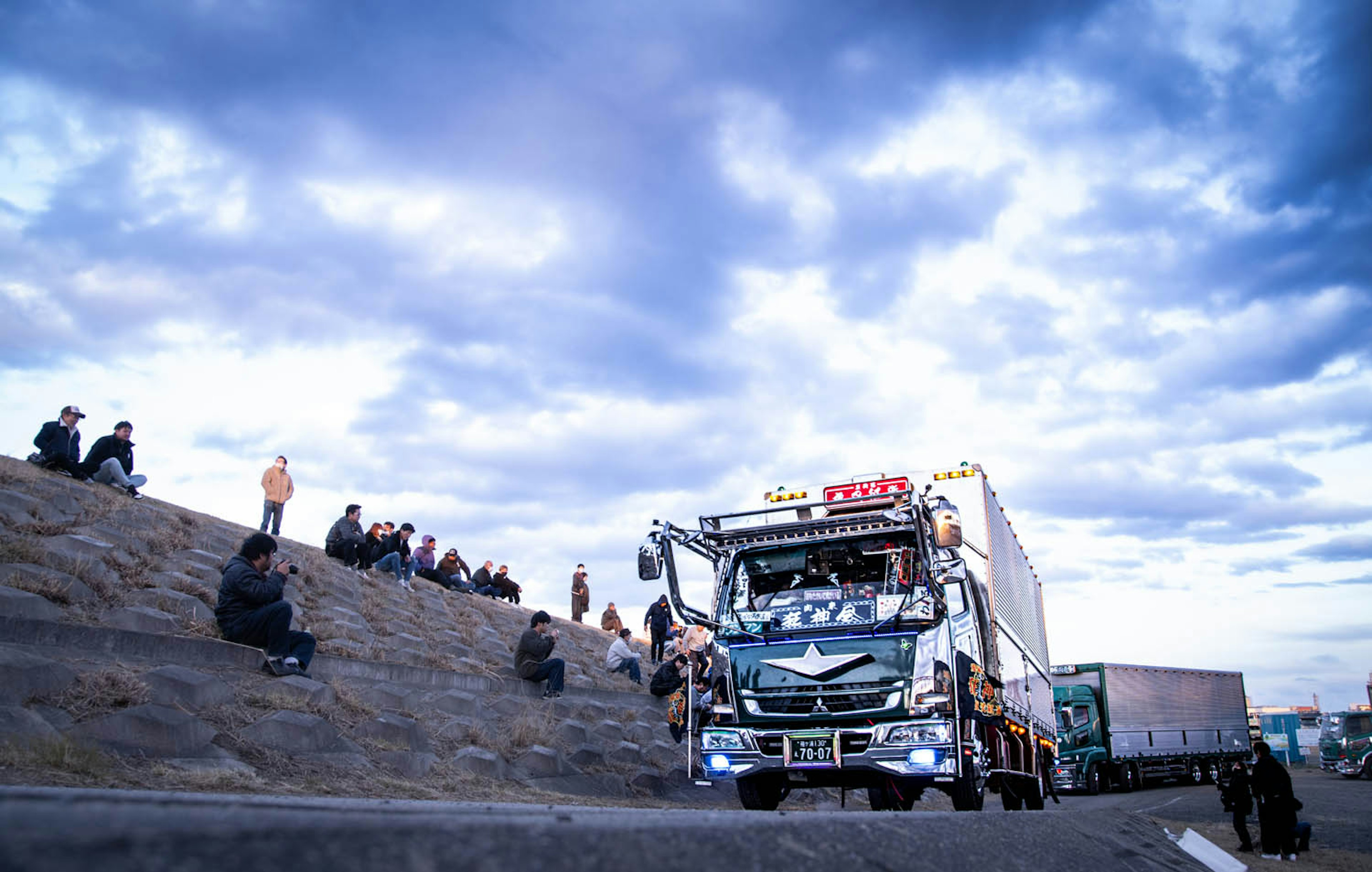 A truck on a highway with people sitting on the embankment