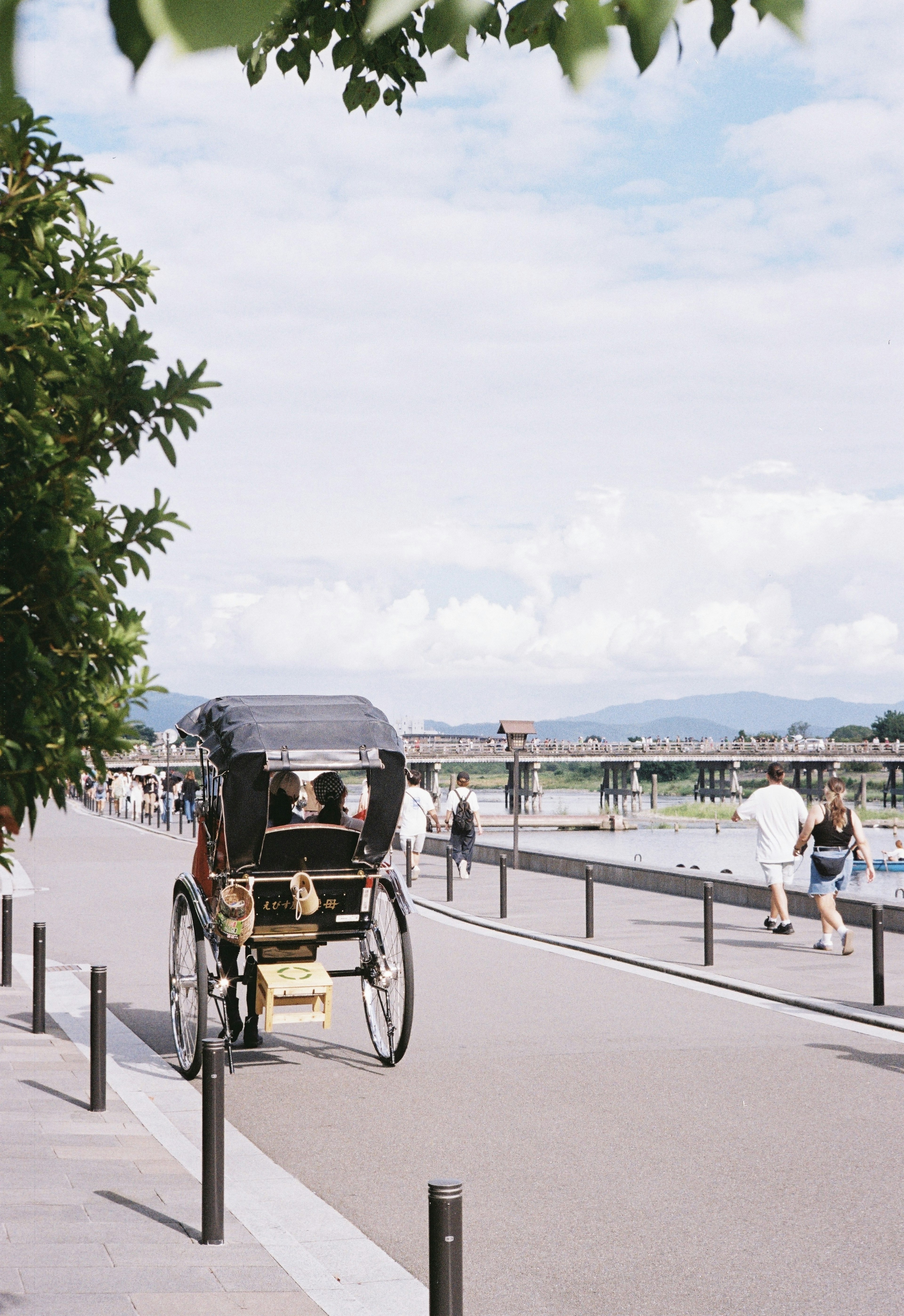 Rickshaw along a riverside path with people walking