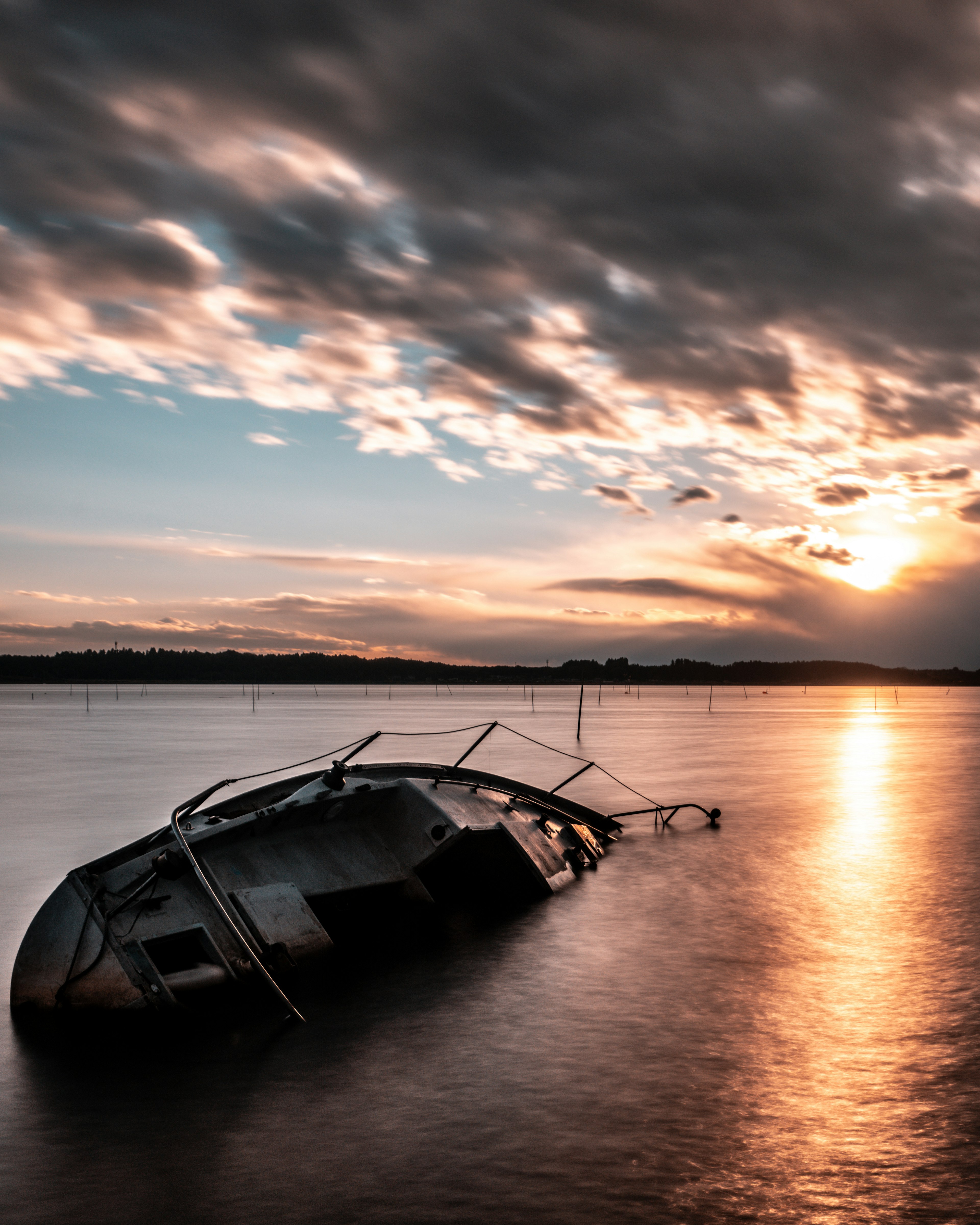 Sebuah perahu yang tenggelam di perairan tenang saat matahari terbenam