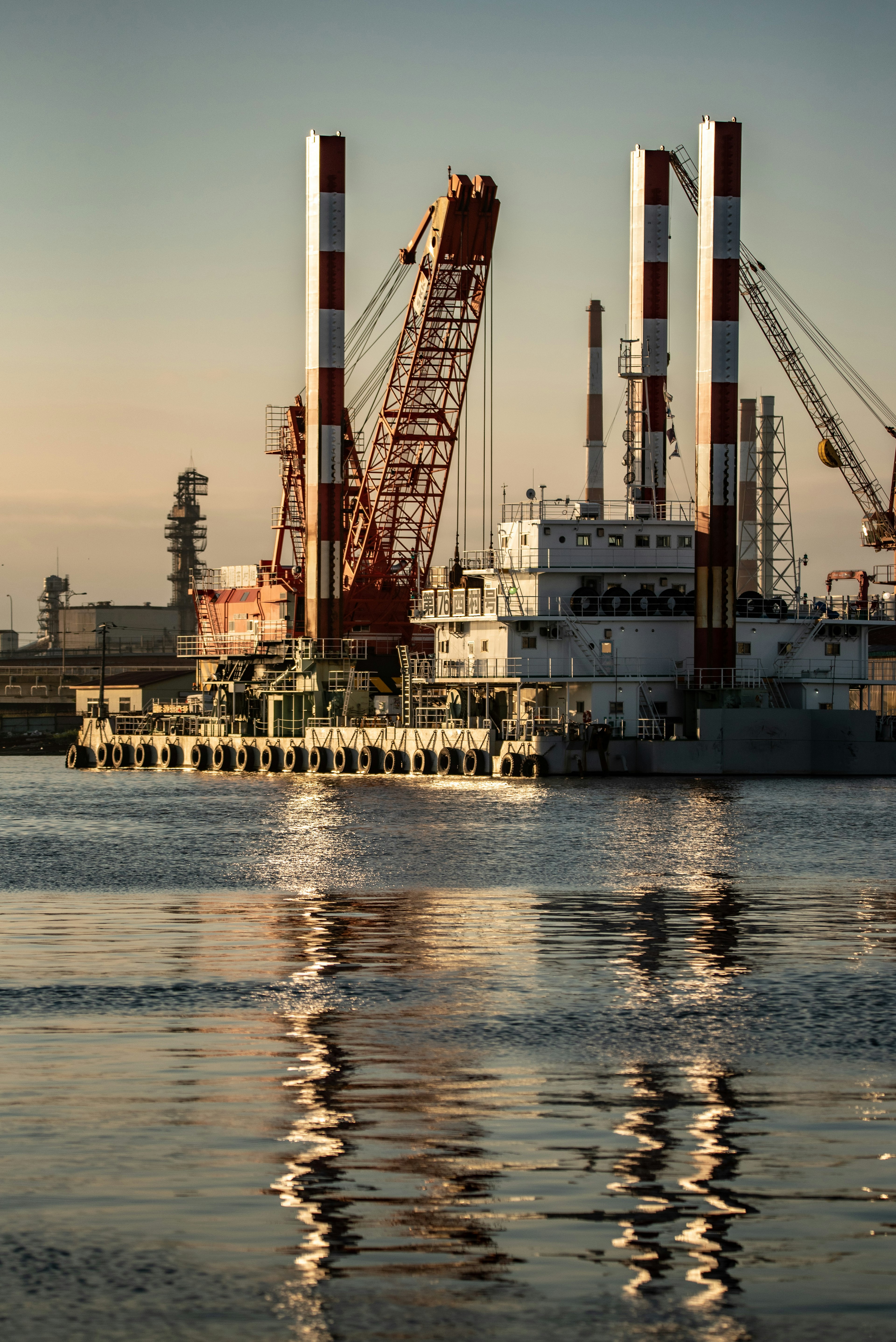 View of cranes and a ship on the water soft dawn light reflecting on the surface