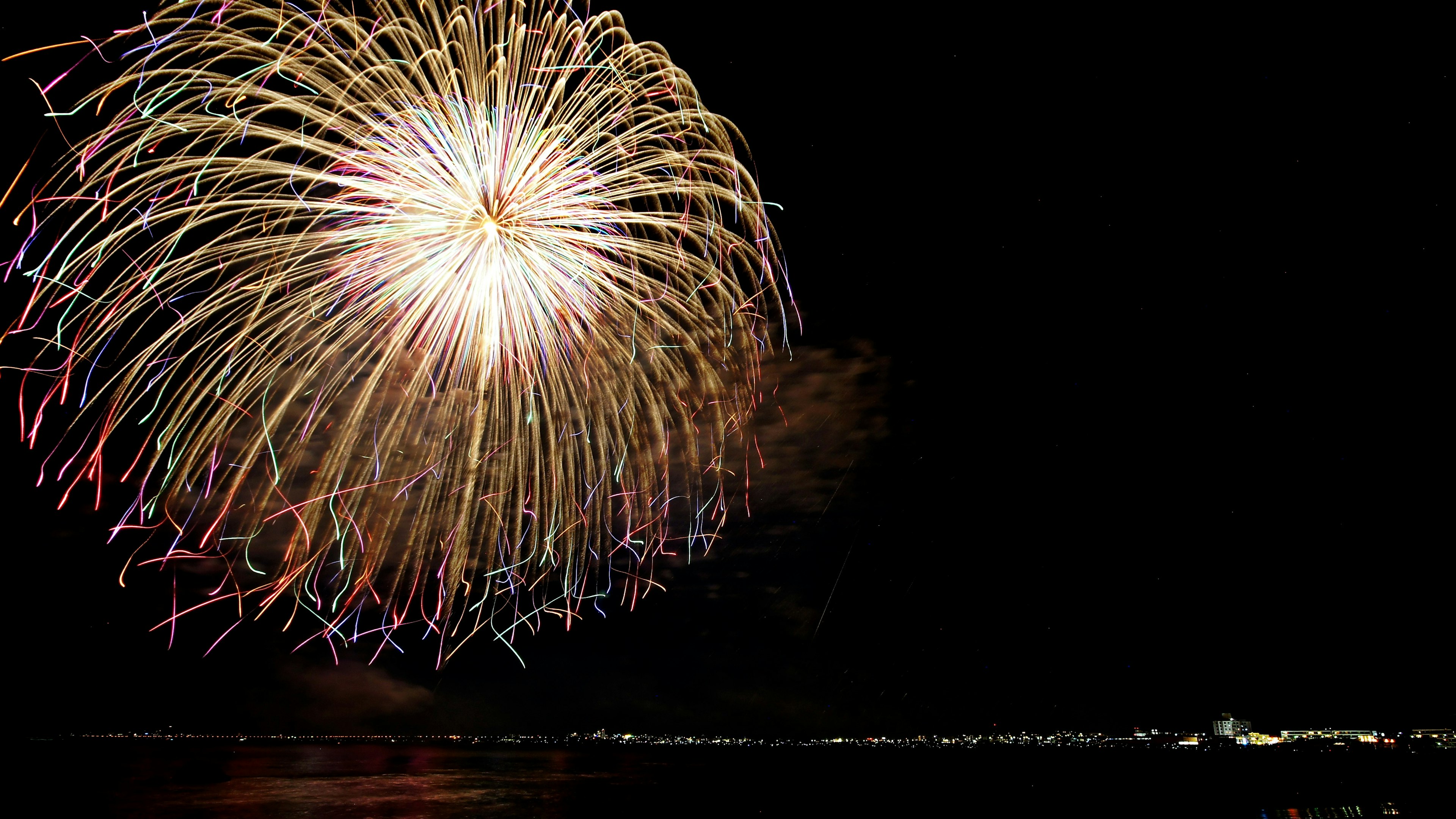 A beautiful display of fireworks in the night sky with a coastline in the background