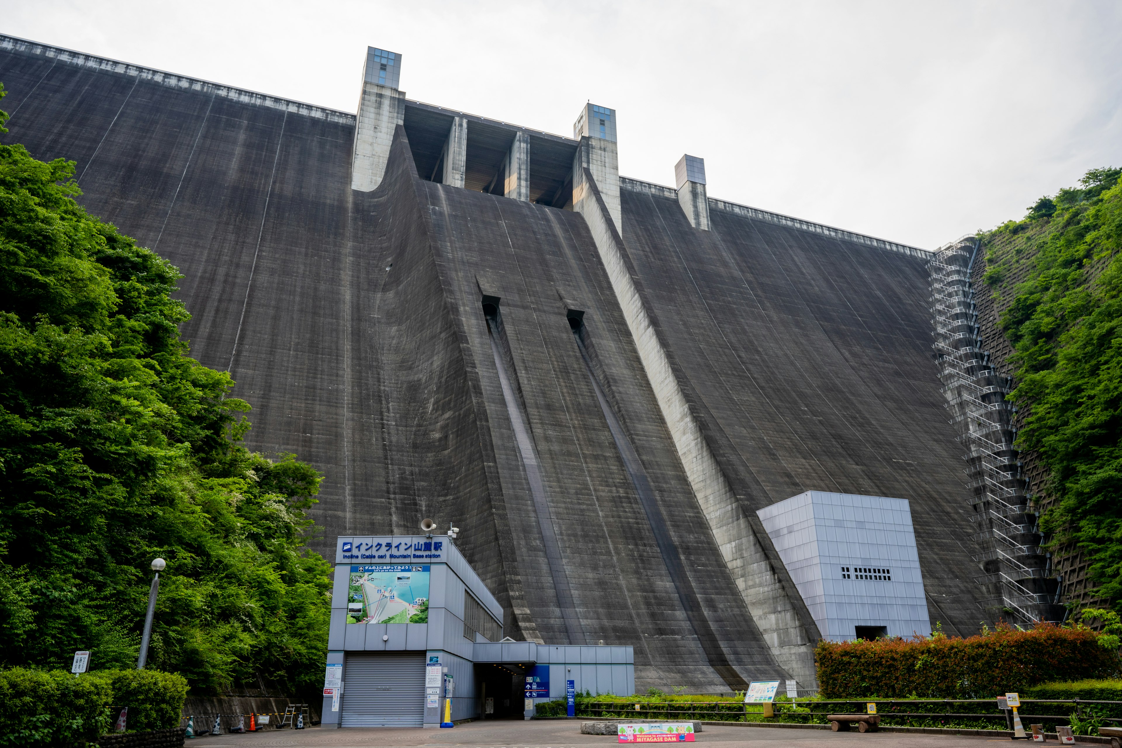 Large concrete dam with steep slopes surrounded by lush greenery