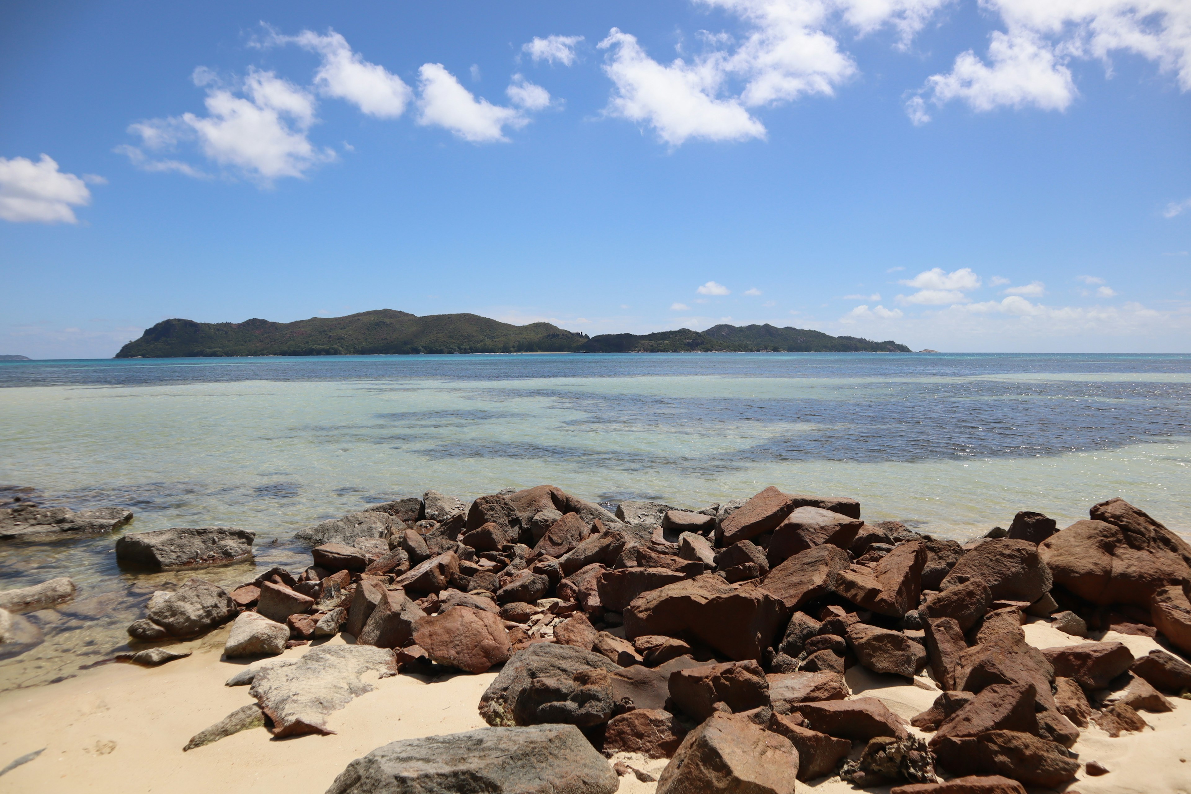 Schöne Küstenlandschaft mit blauem Himmel und weißen Wolken felsiger Strand mit verstreuten Steinen und einer fernen Insel