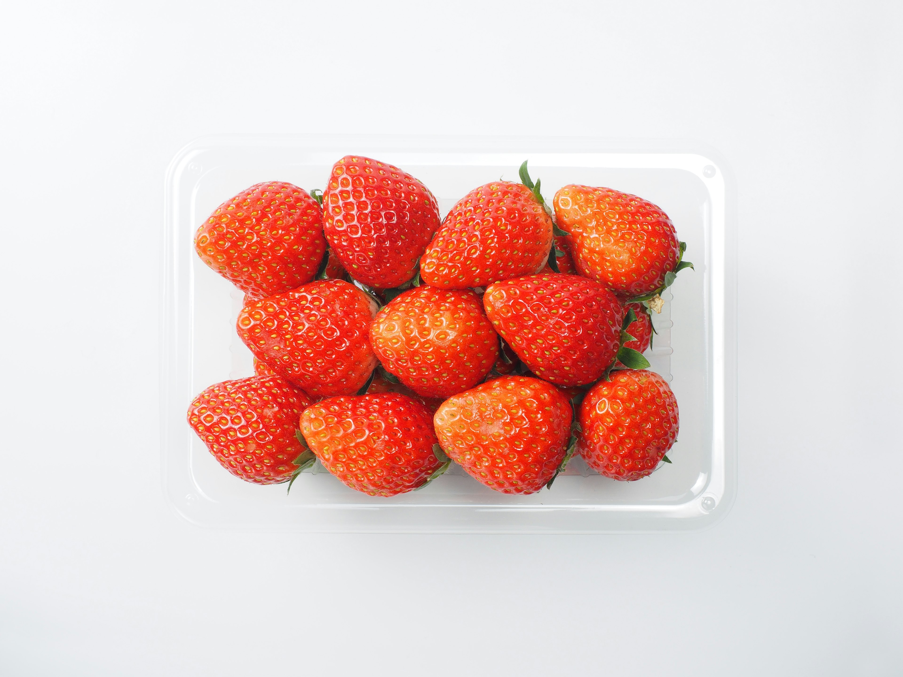 A pile of fresh strawberries in a clear plastic container