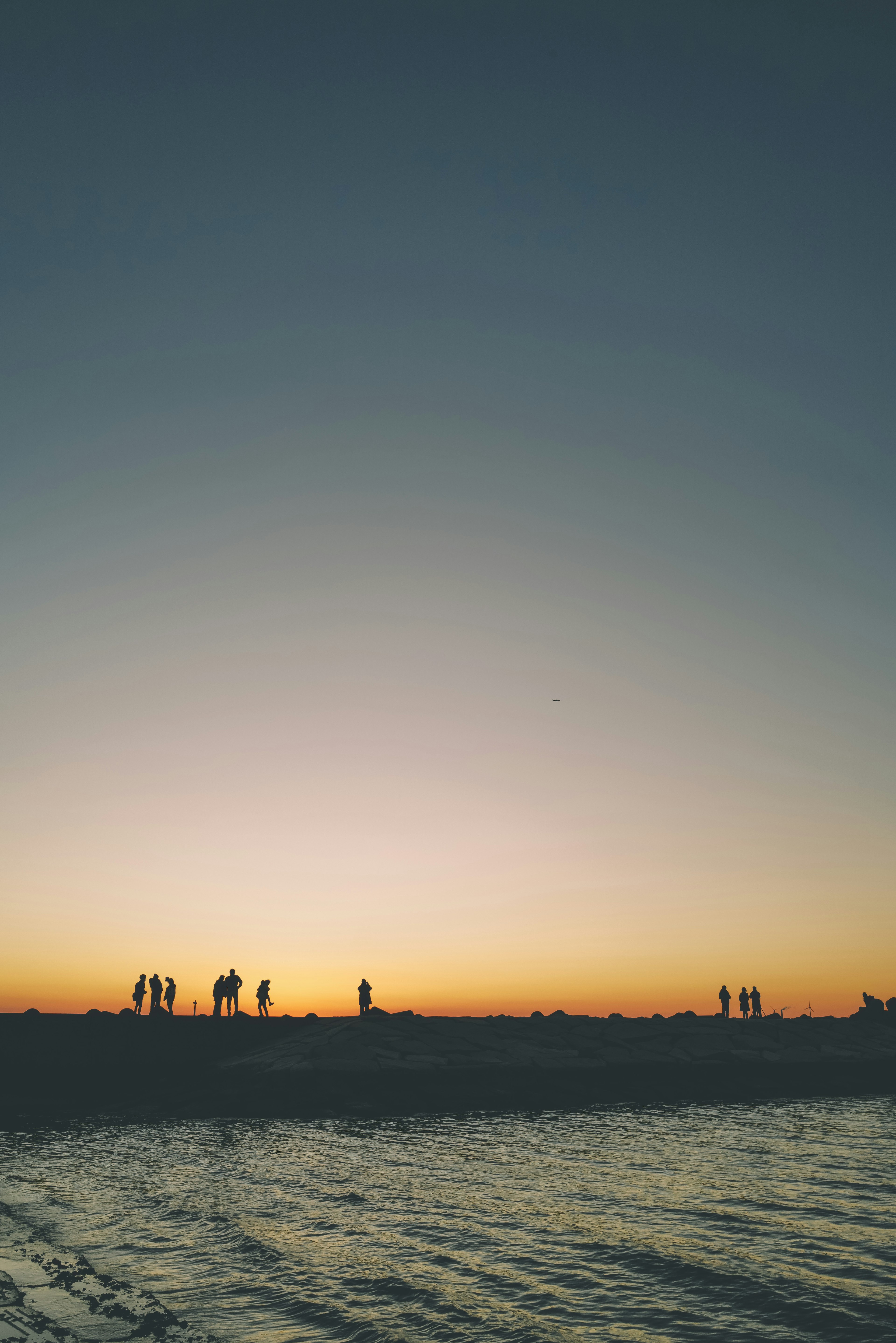 Siluetas de personas en una playa al atardecer con aguas tranquilas